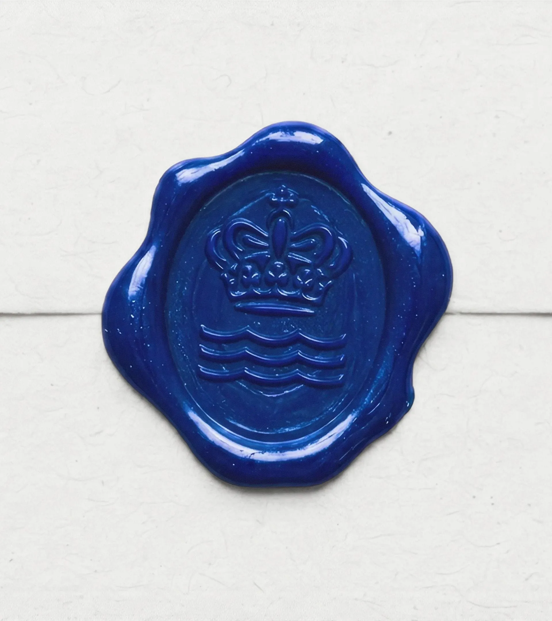 Sello de lacre azul con una corona y tres olas en relieve sobre un sobre de papel claro