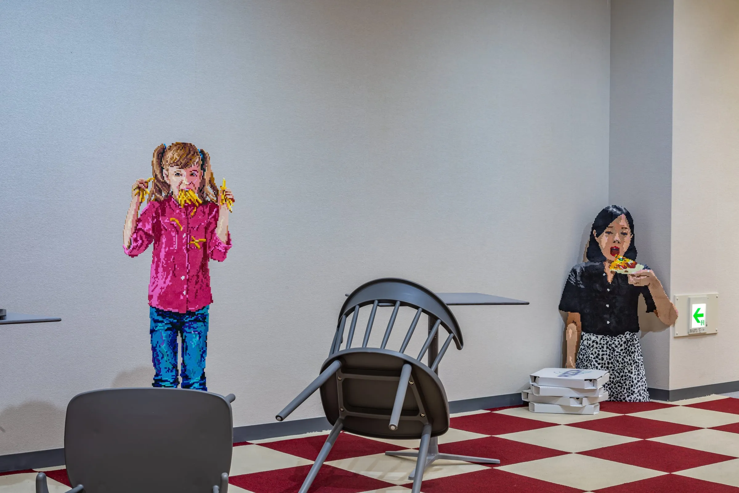 Dos figuras pixeladas en el local de comida rápida: una niña con las manos llenas de patatas y una mujer comiendo una porción de pizza