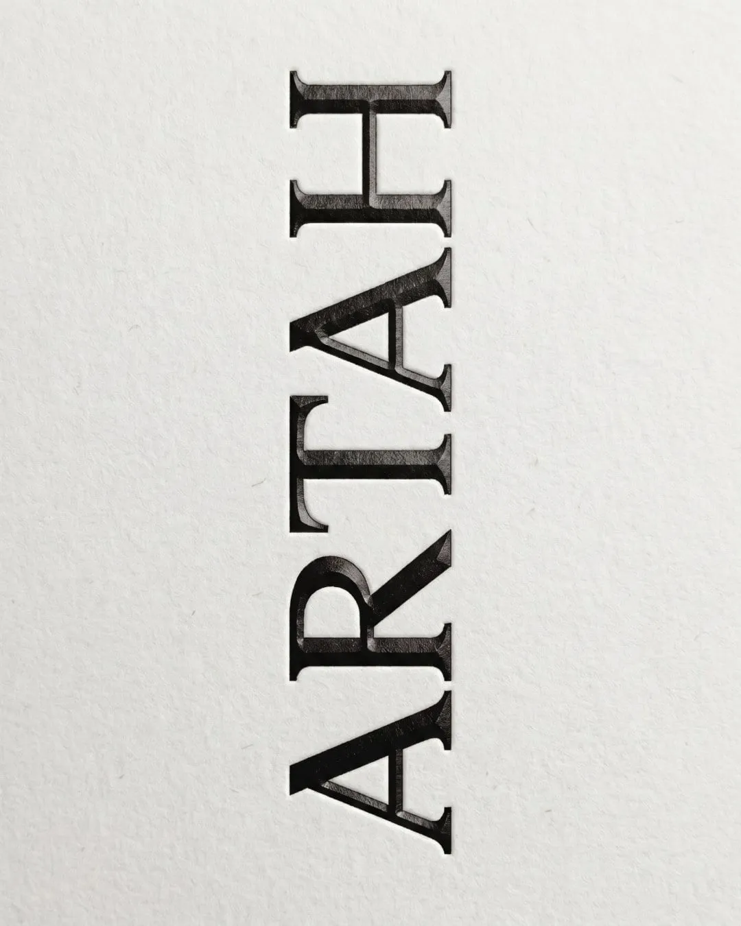 Logotipo de Artah en vertical, con letras serif de remates triangulares y relieve, sobre papel blanco con textura