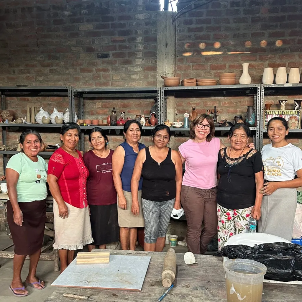 Ana Illueca junto a las ocho mujeres del taller de cerámica de La Encantada, en Chulucanas, Perú, delante de estanterías con piezas de barro