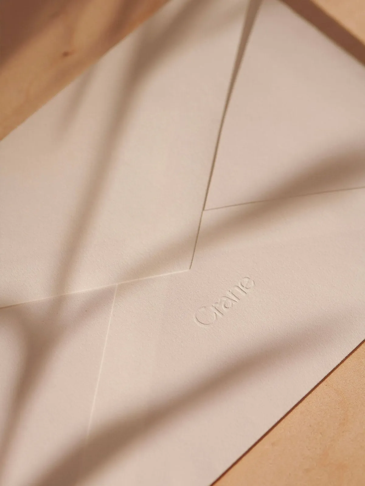 Sobre de papel de algodón color crema con el logotipo de Crane en relieve seco, sin tinta, iluminado con luz cálida