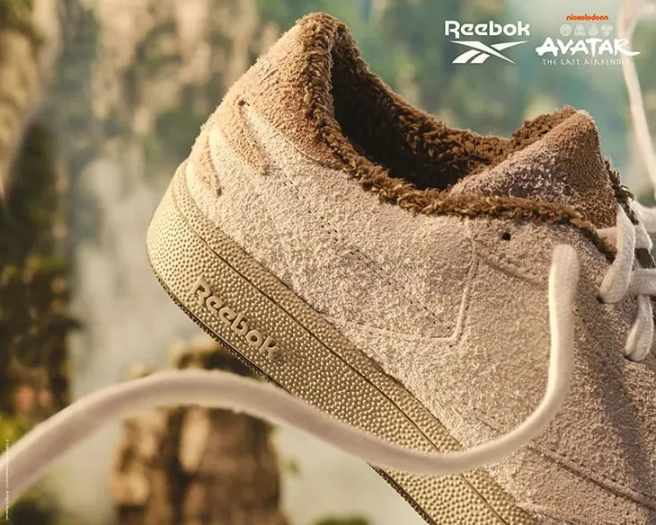 Zapatilla Club C 85 de ante peludo beige con cuello de felpa marrón, flotando ante un paisaje de montañas entre la niebla