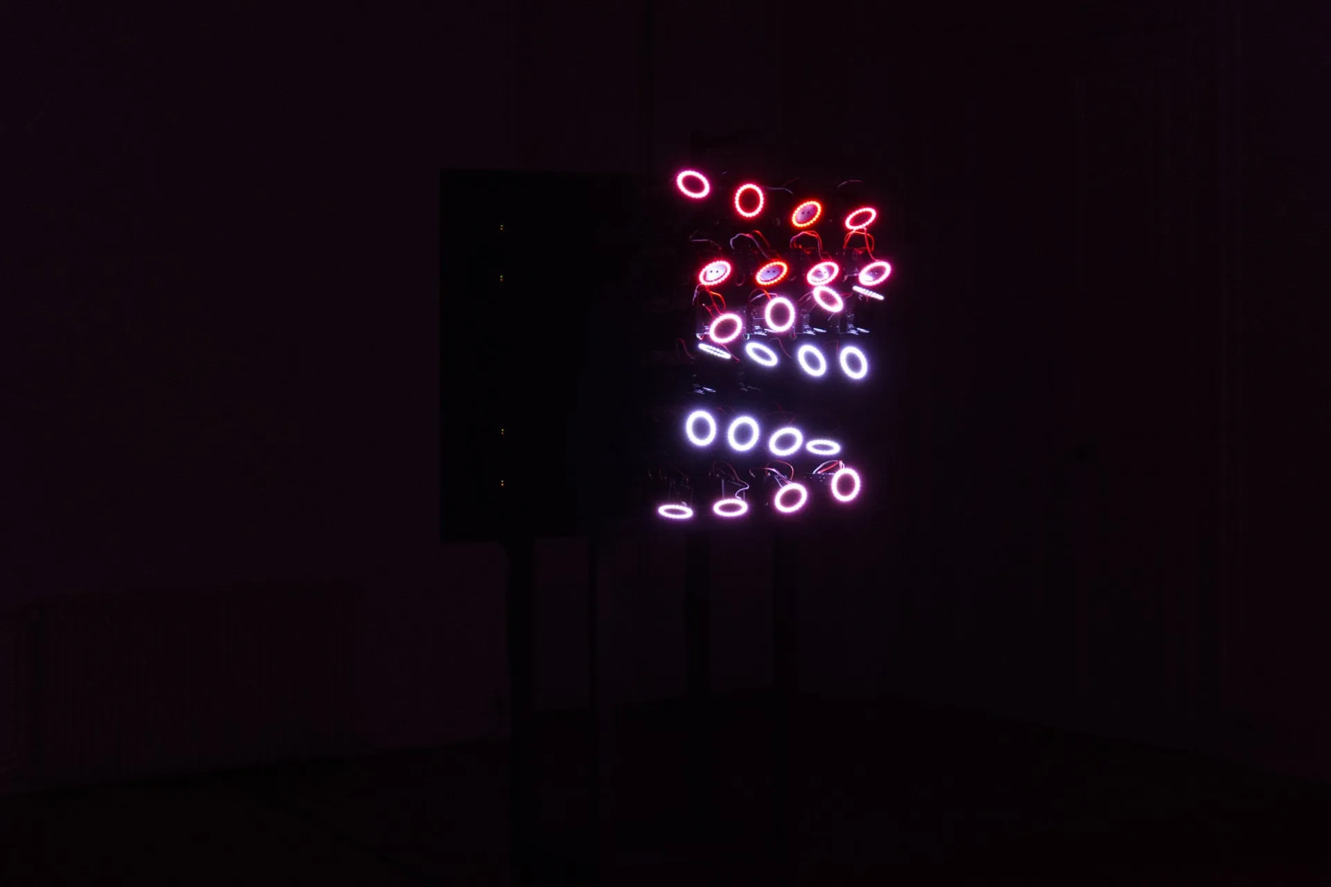 Vista lateral de la escultura con los anillos de luz saliendo de una estructura negra con motores y cables