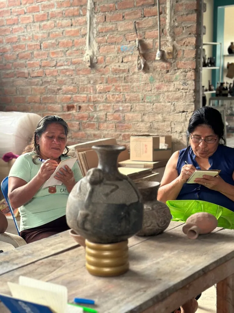 Dos mujeres artesanas de AMAM tomando notas junto a vasijas de cerámica tradicional en una mesa de un taller de Chulucanas