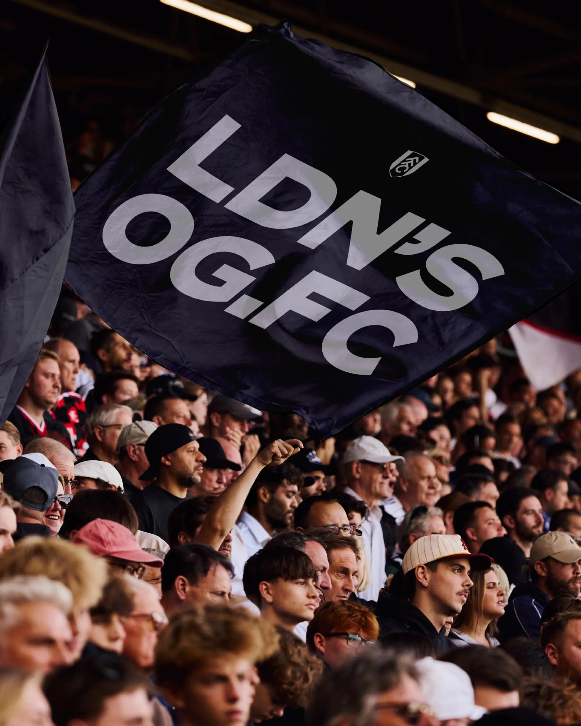 Una bandera azul marino ondea sobre la grada con las letras grises «LDN’s OG.FC» y el escudo del Fulham