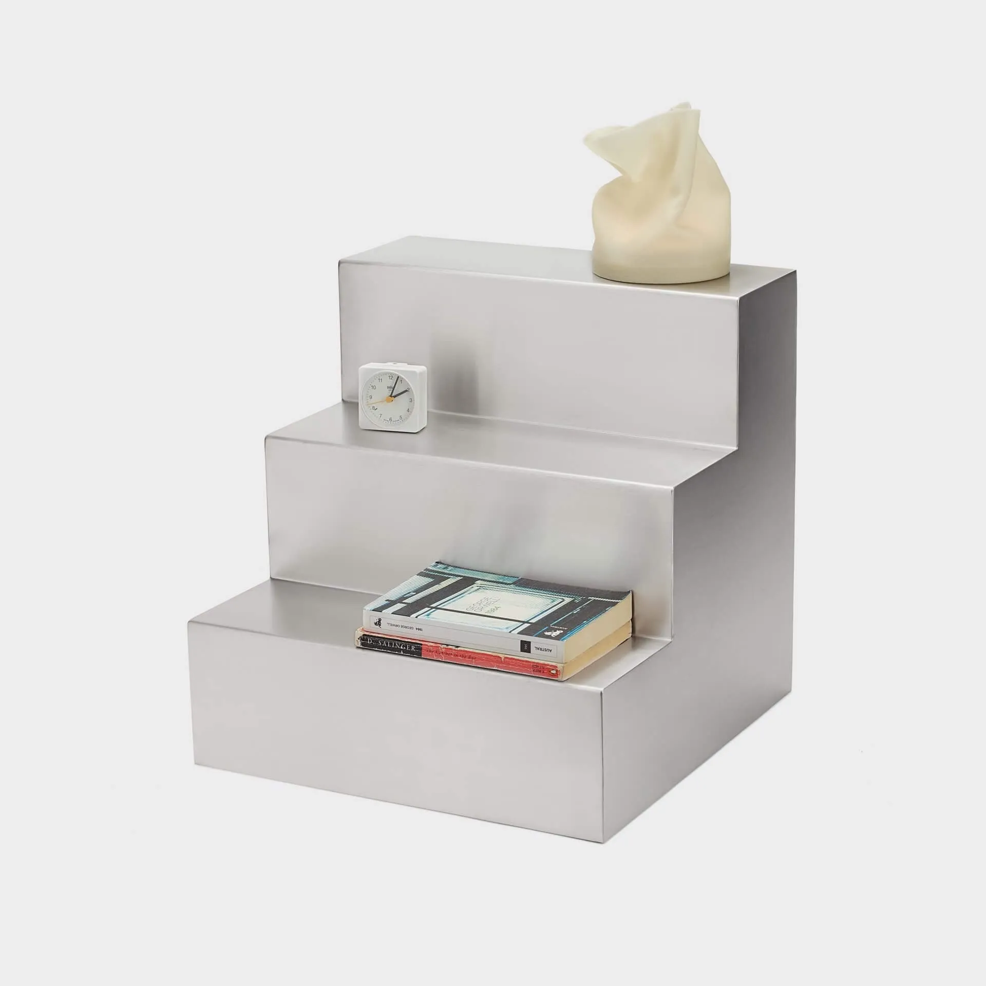 Mesa auxiliar Escala con un despertador blanco, dos libros apilados y una vela de cera crema en los tres peldaños