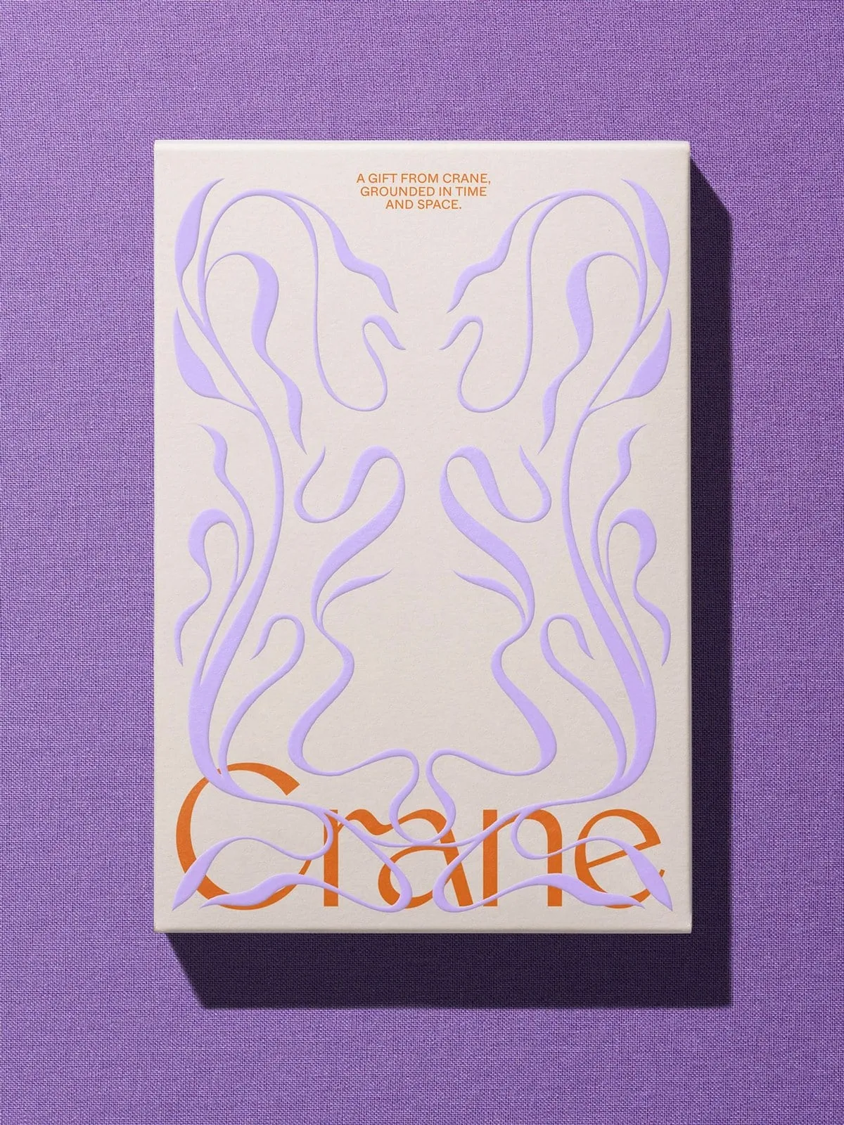 Caja crema sobre tela violeta, con adornos de plantas en lila en relieve y el nombre Crane en naranja