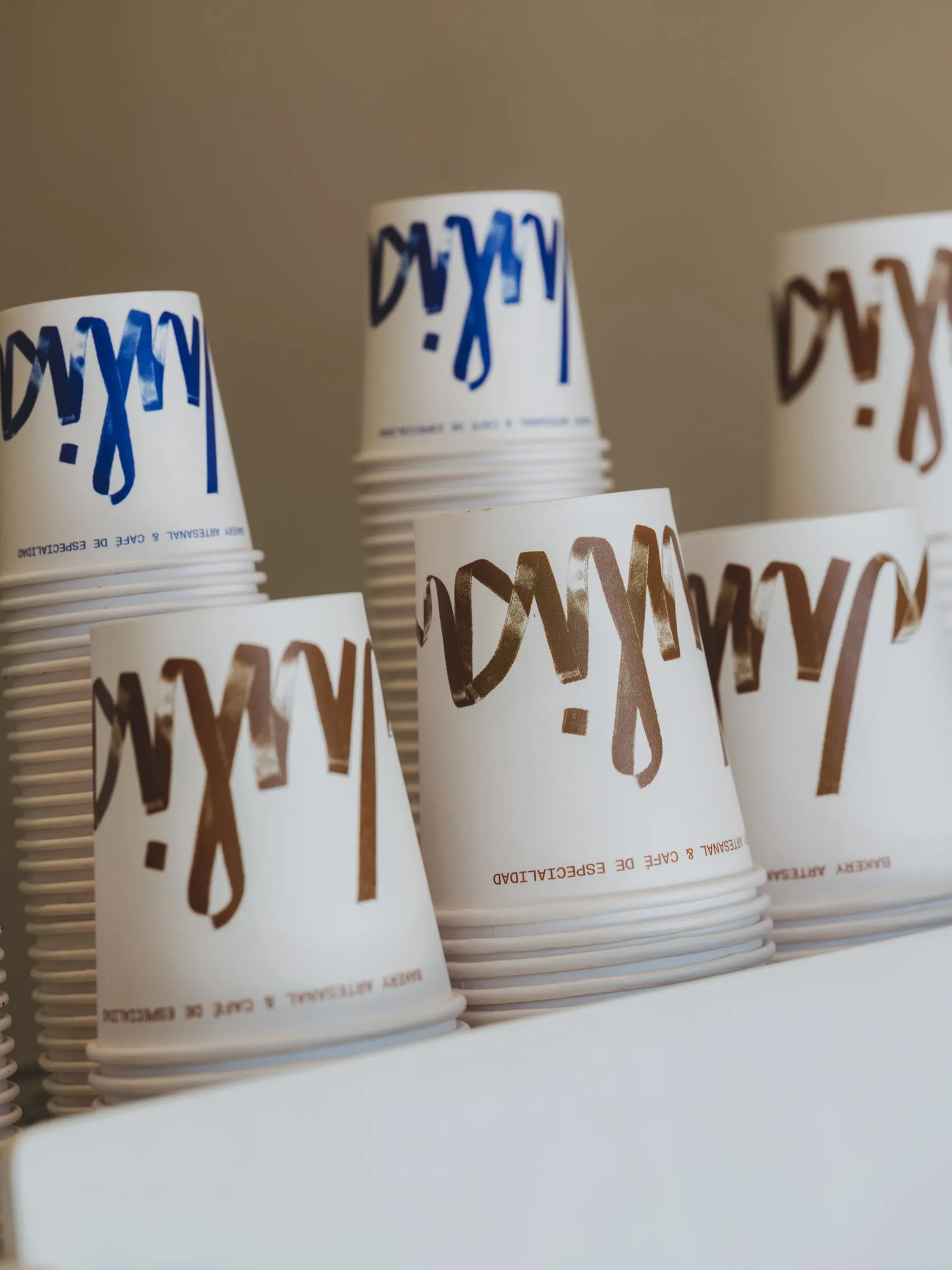 Pila de vasos de papel con el logotipo de Julia en azul y en marrón, apilados y vistos de lado