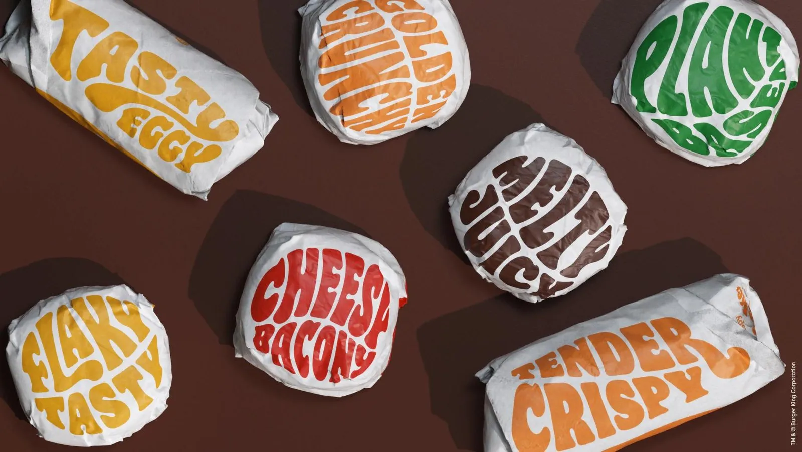Envoltorios de Burger King vistos desde arriba sobre fondo marrón, con nombres de bocadillos en letras redondeadas de colores