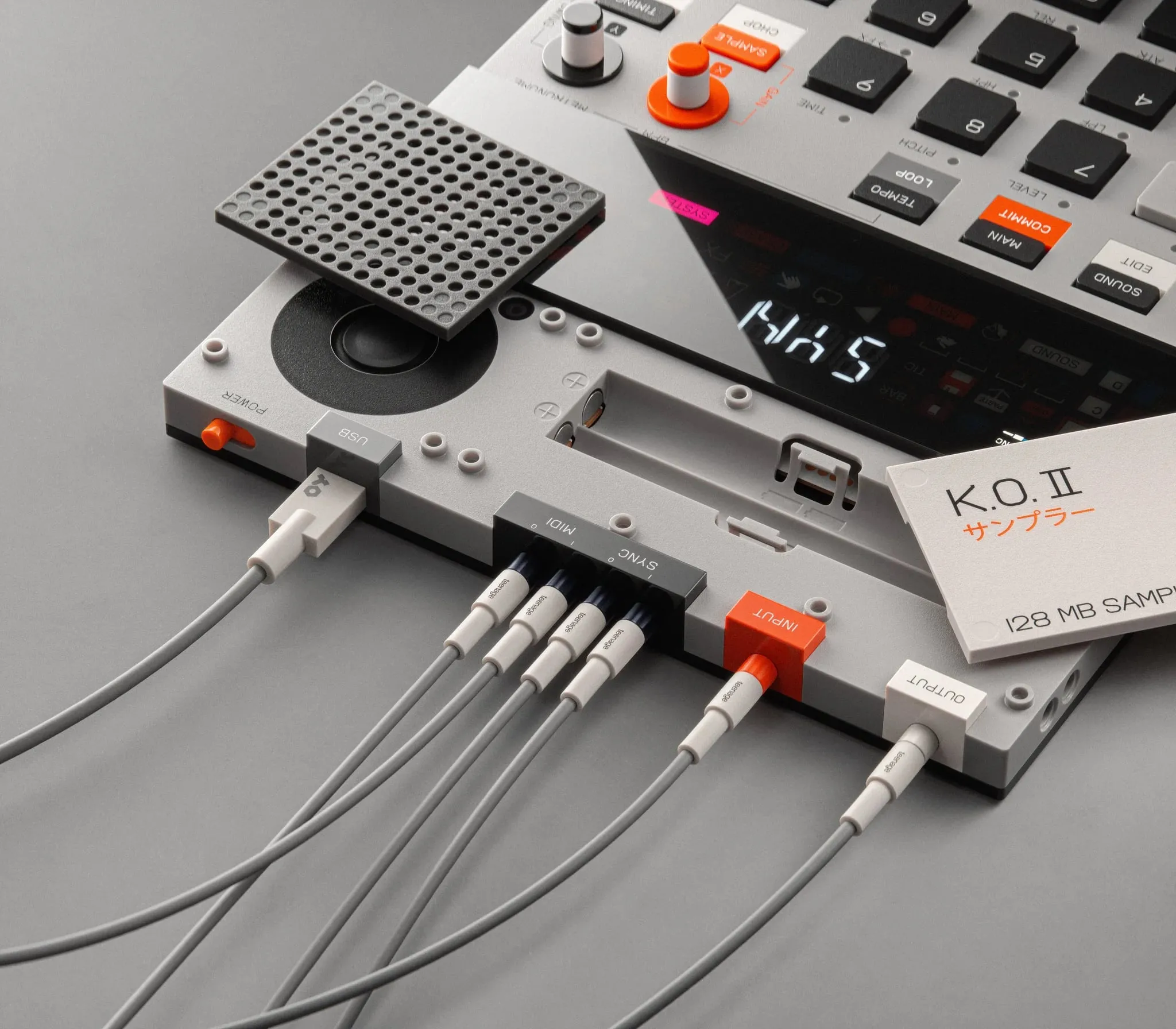 Parte trasera del K.O. II con la tapa del altavoz levantada y varios cables grises conectados a las entradas marcadas como USB, MIDI, Sync, Input y Output