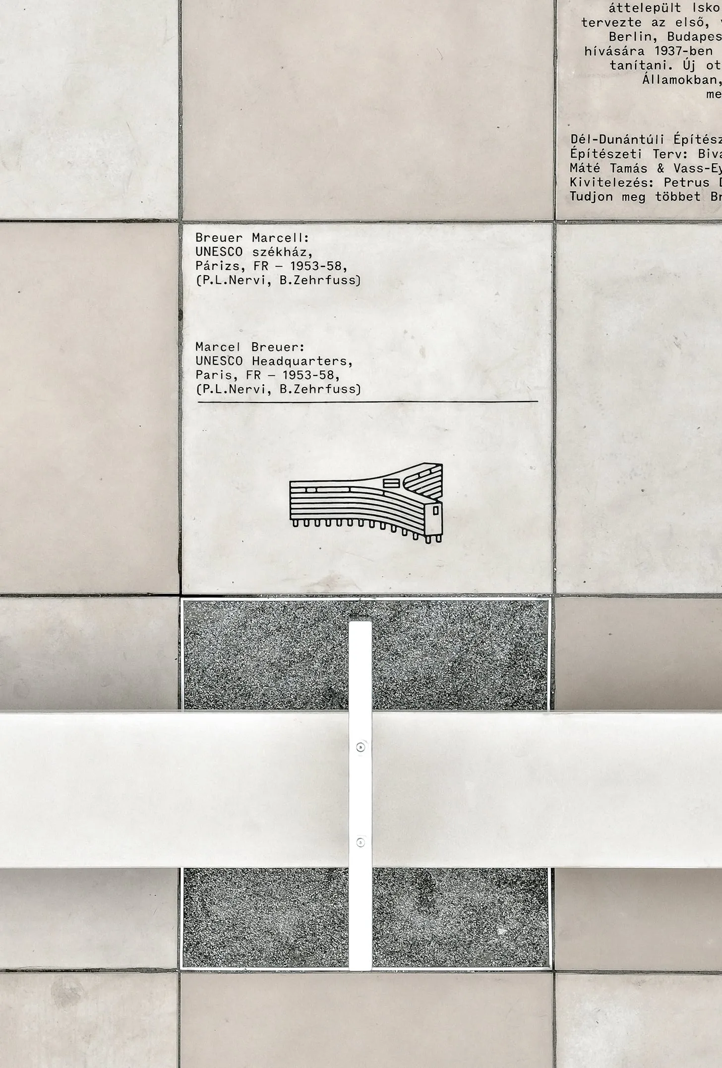 Detalle de una baldosa con el dibujo de la sede de la UNESCO en París y, debajo, un pie del banco