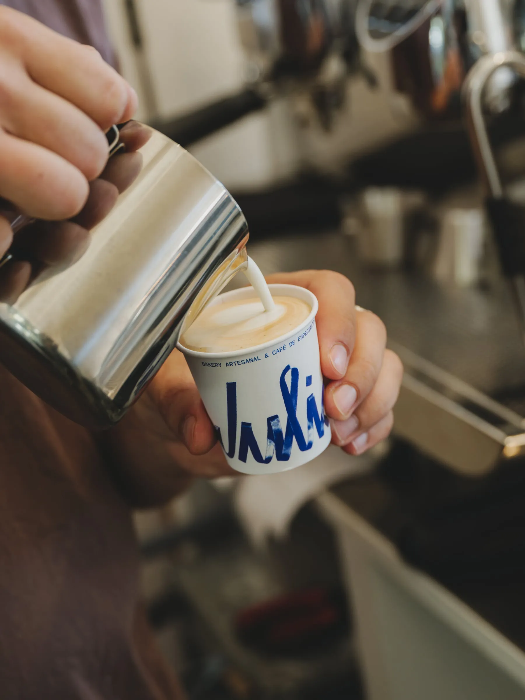 Barista sirviendo leche en un vaso de papel blanco con el logotipo de Julia en azul cobalto