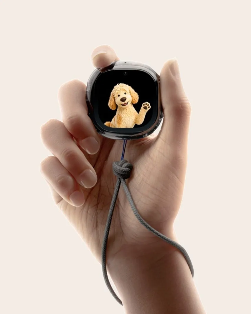 Una mano sostiene el Muse Charm de Meta con la pantalla mostrando un perrito labradoodle de peluche que saluda con la pata