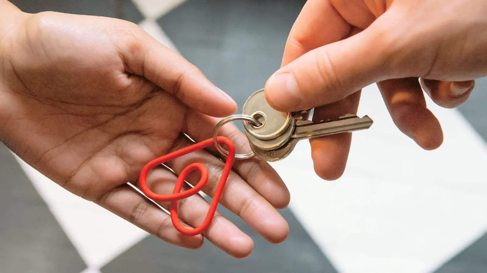 Una mano entrega unas llaves a otra con un llavero rojo con la forma del símbolo Bélo de Airbnb