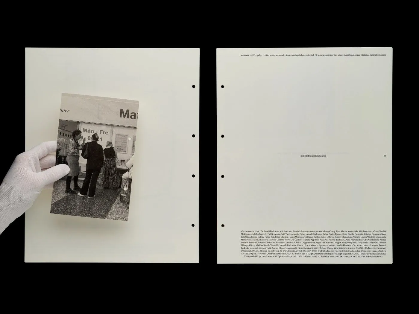 Una mano con guante blanco sujeta una fotografía en blanco y negro de tres personas ante un mostrador, sobre una hoja de papel crudo