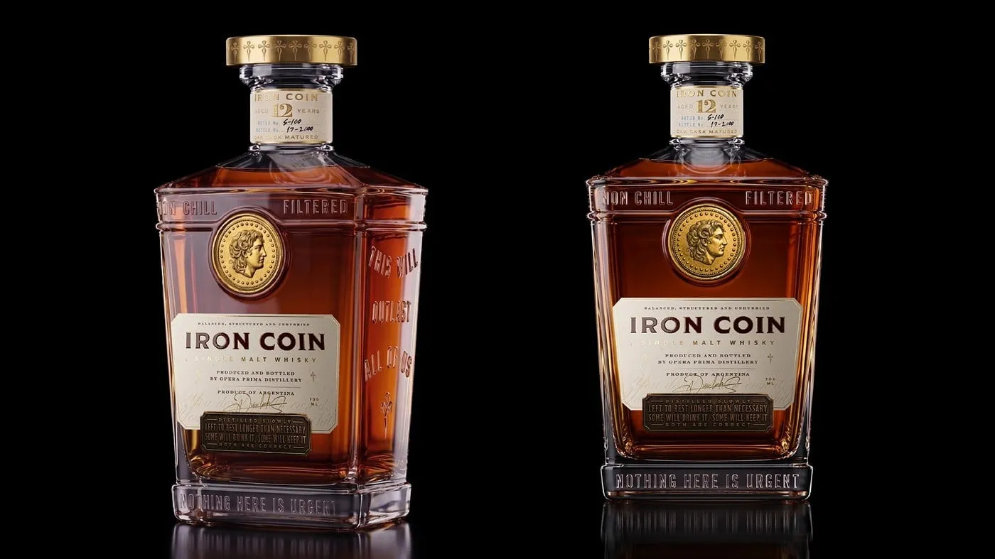Dos botellas de whisky Iron Coin sobre fondo negro, con etiqueta crema, moneda dorada en el hombro y tapón de latón