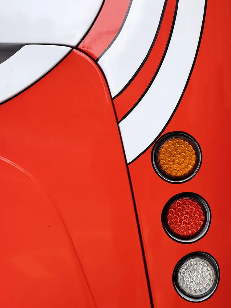 Trasera roja de un autobús con franjas blancas curvas y tres pilotos redondos en vertical
