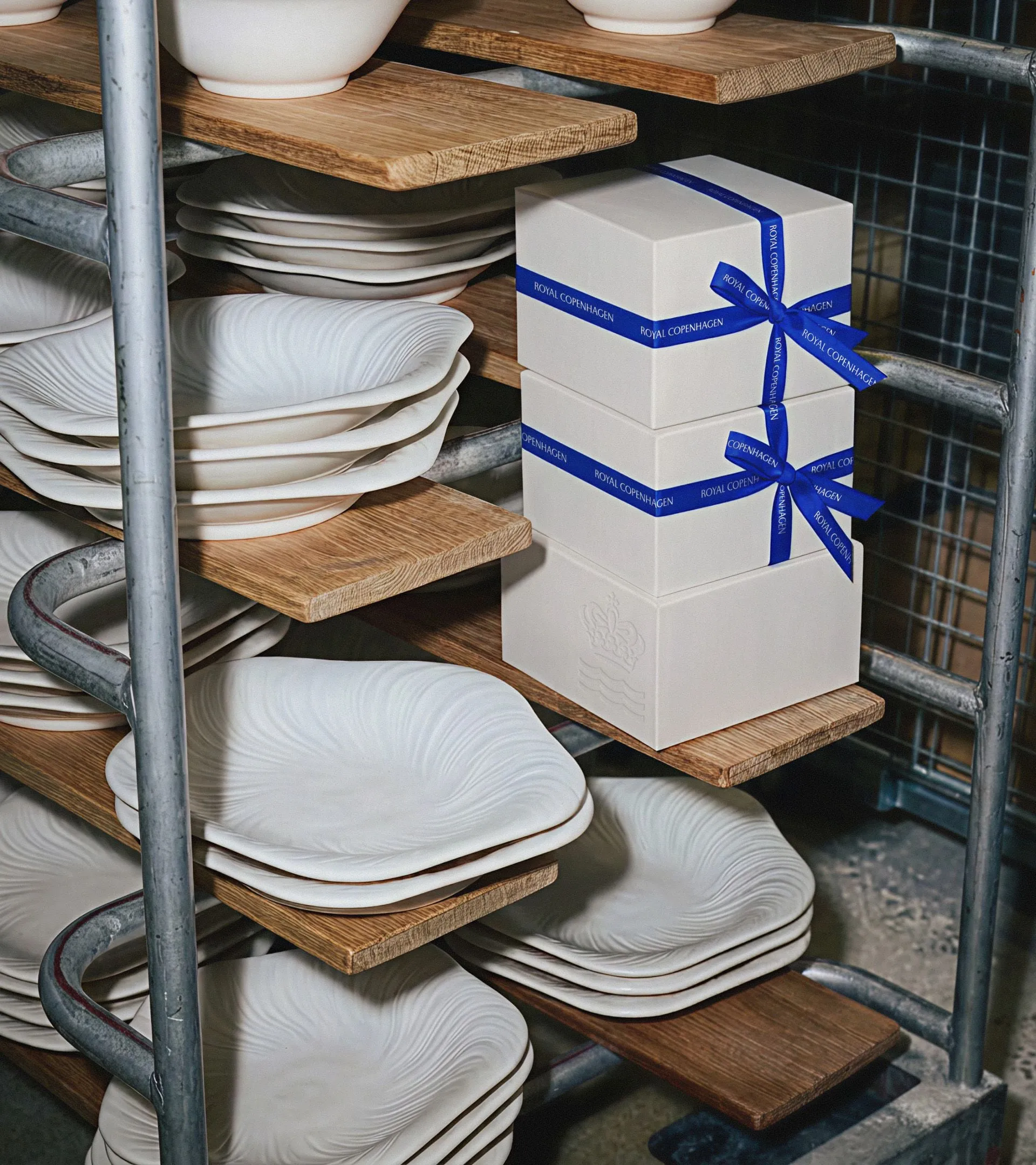 Estantería de fábrica con platos blancos de relieve ondulado y cajas de regalo atadas con una cinta azul con el nombre de la marca