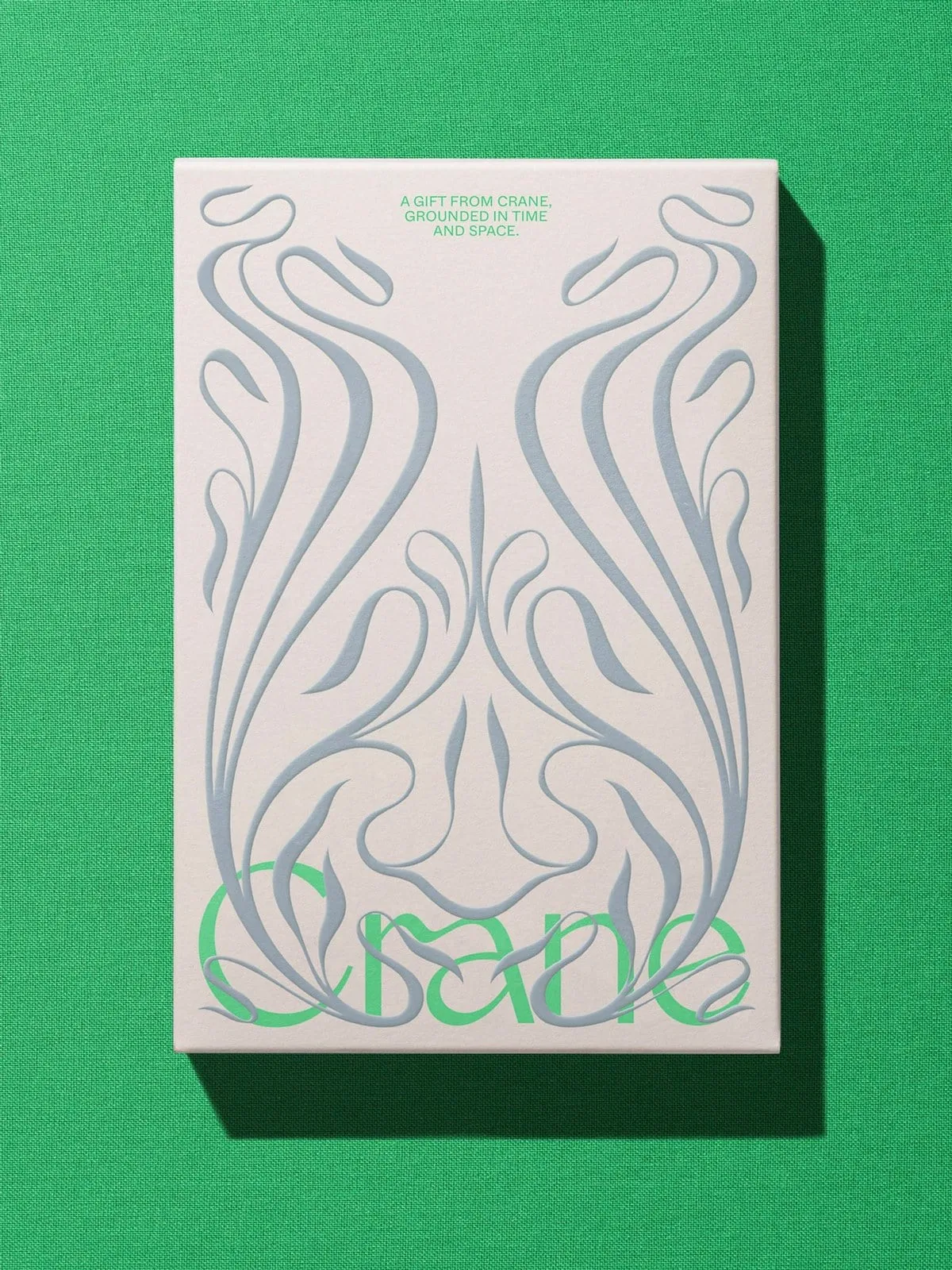 Caja crema sobre tela verde con adornos de plantas en gris azulado en relieve y el nombre Crane en verde claro