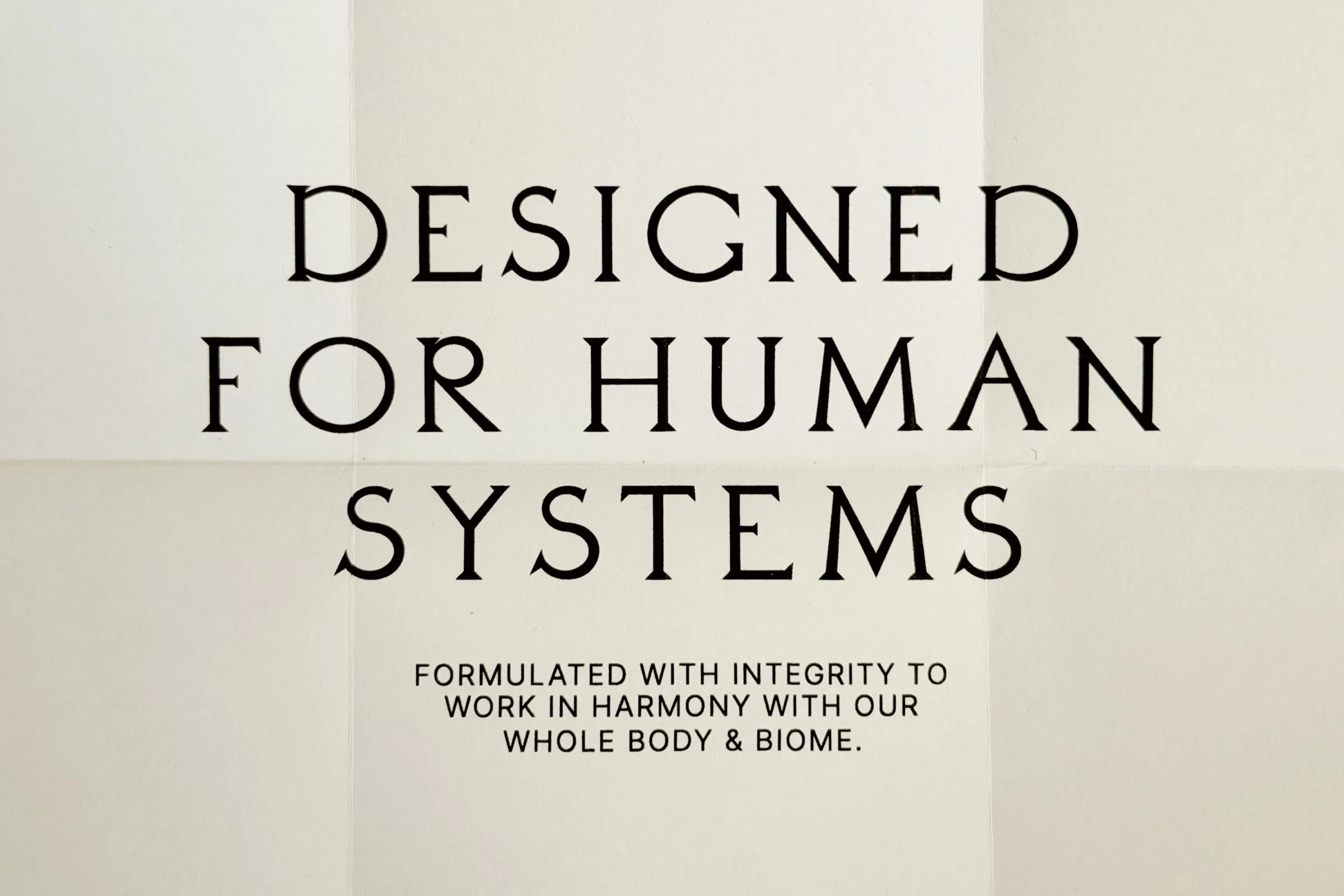 Cartel tipográfico en letras serif con el texto Designed for human systems sobre fondo de papel crema plegado