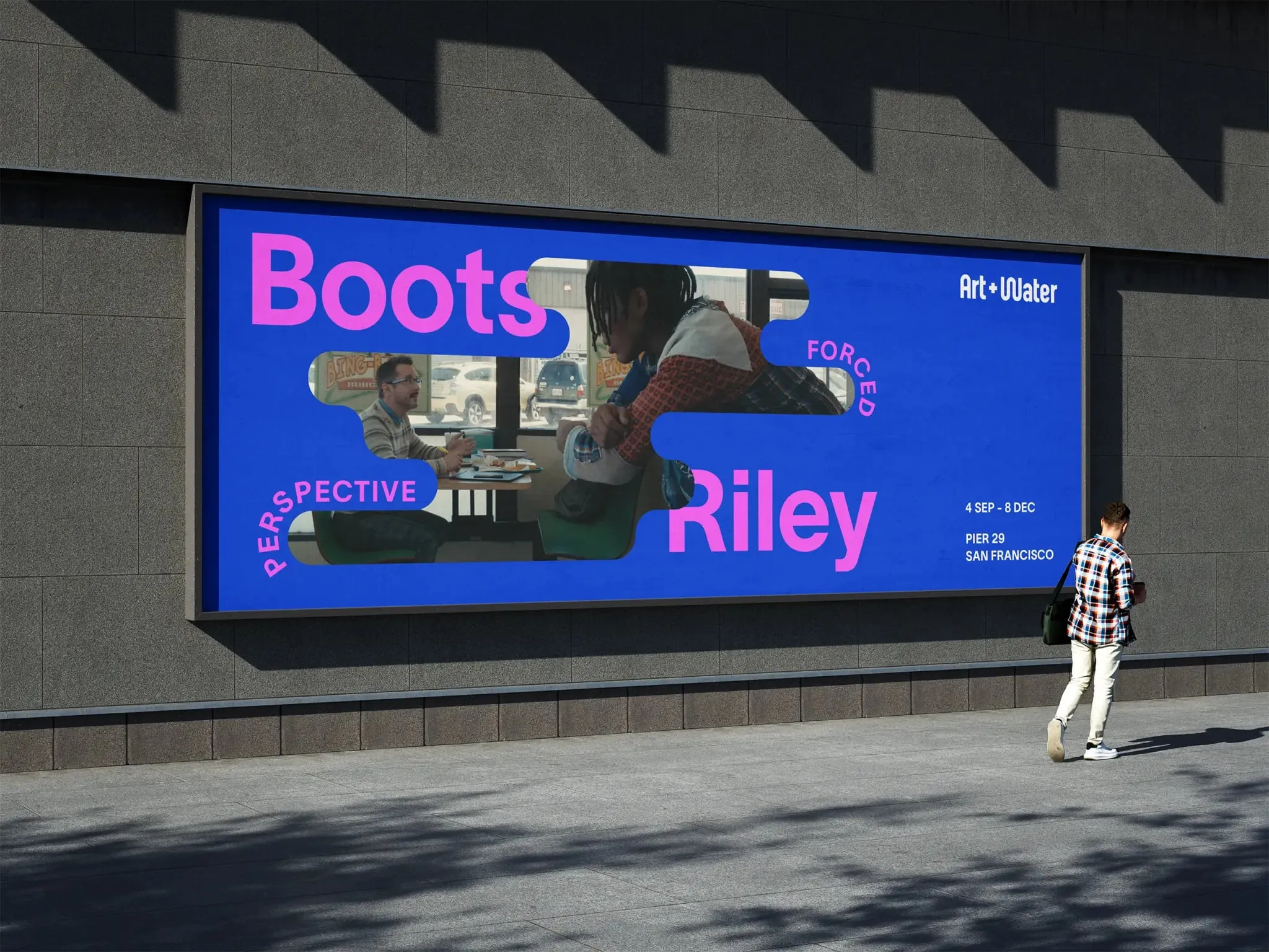 Valla publicitaria azul con la foto de dos personas en una mesa dentro de un hueco curvo y los nombres «Boots» y «Riley» en fucsia