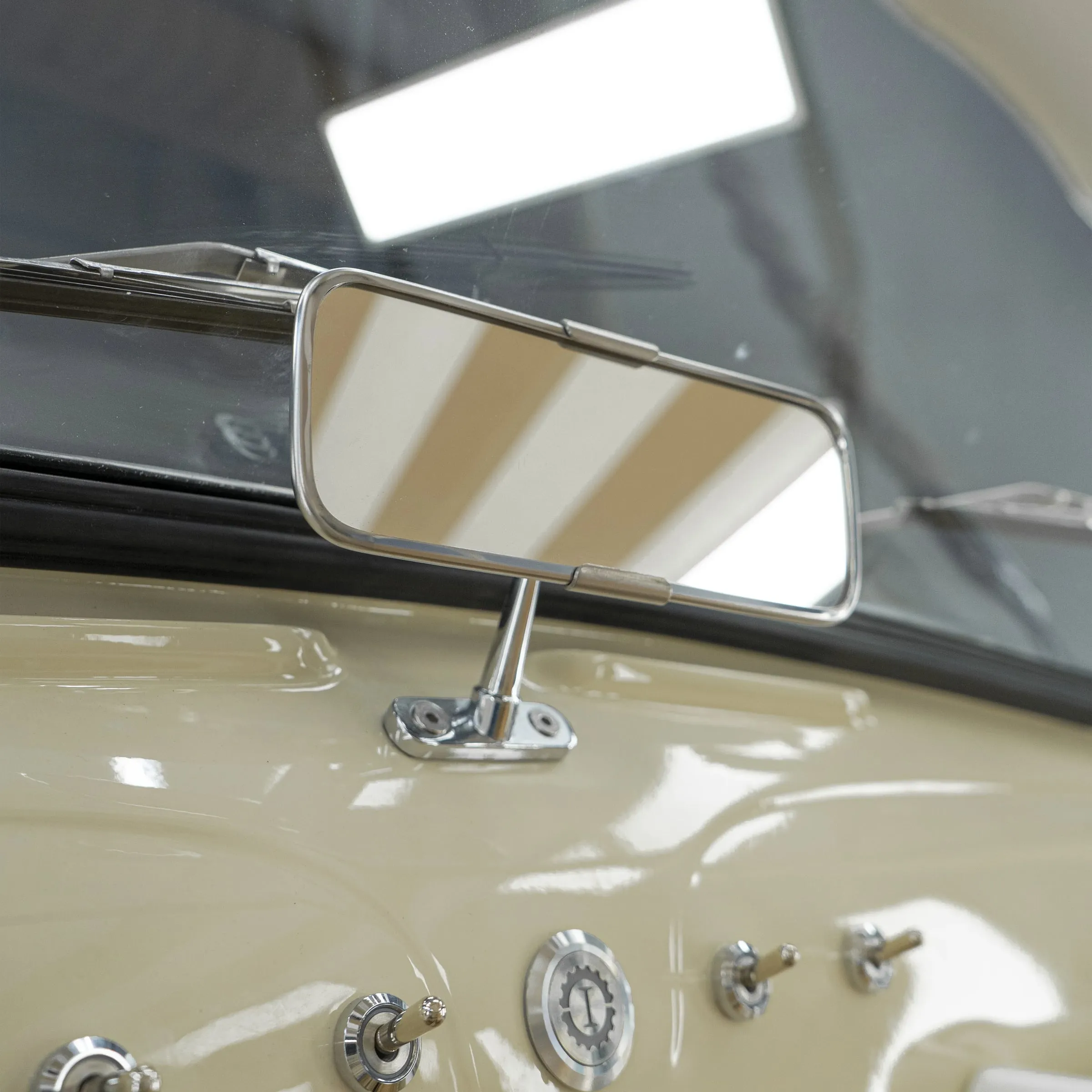 Retrovisor central cromado sobre el salpicadero crema, con el reflejo de unas rayas beige y varios interruptores de palanca debajo