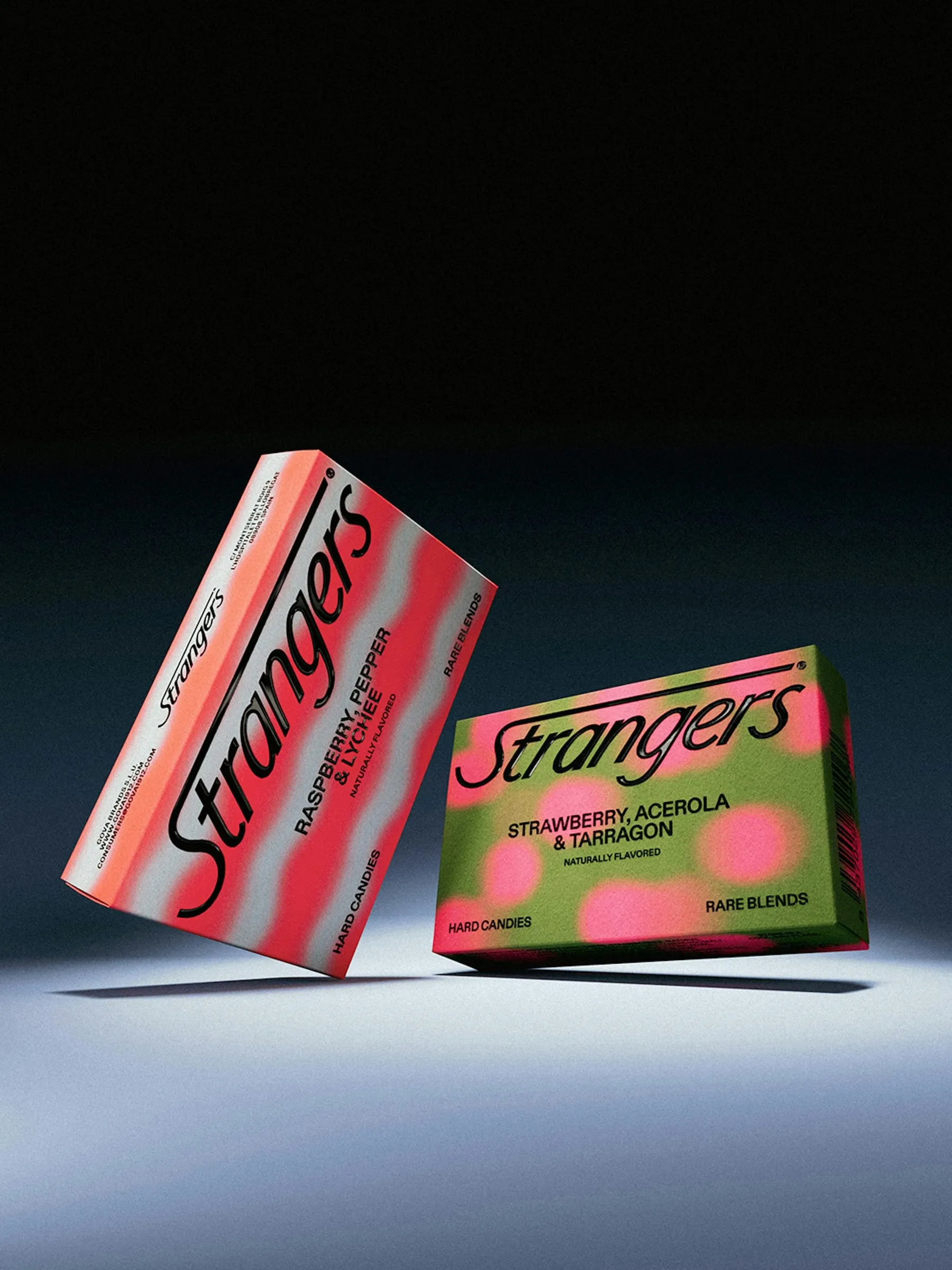Dos cajas de Strangers inclinadas en el aire, una rosa de frambuesa, pimienta y lichi y otra verde de fresa, acerola y estragón