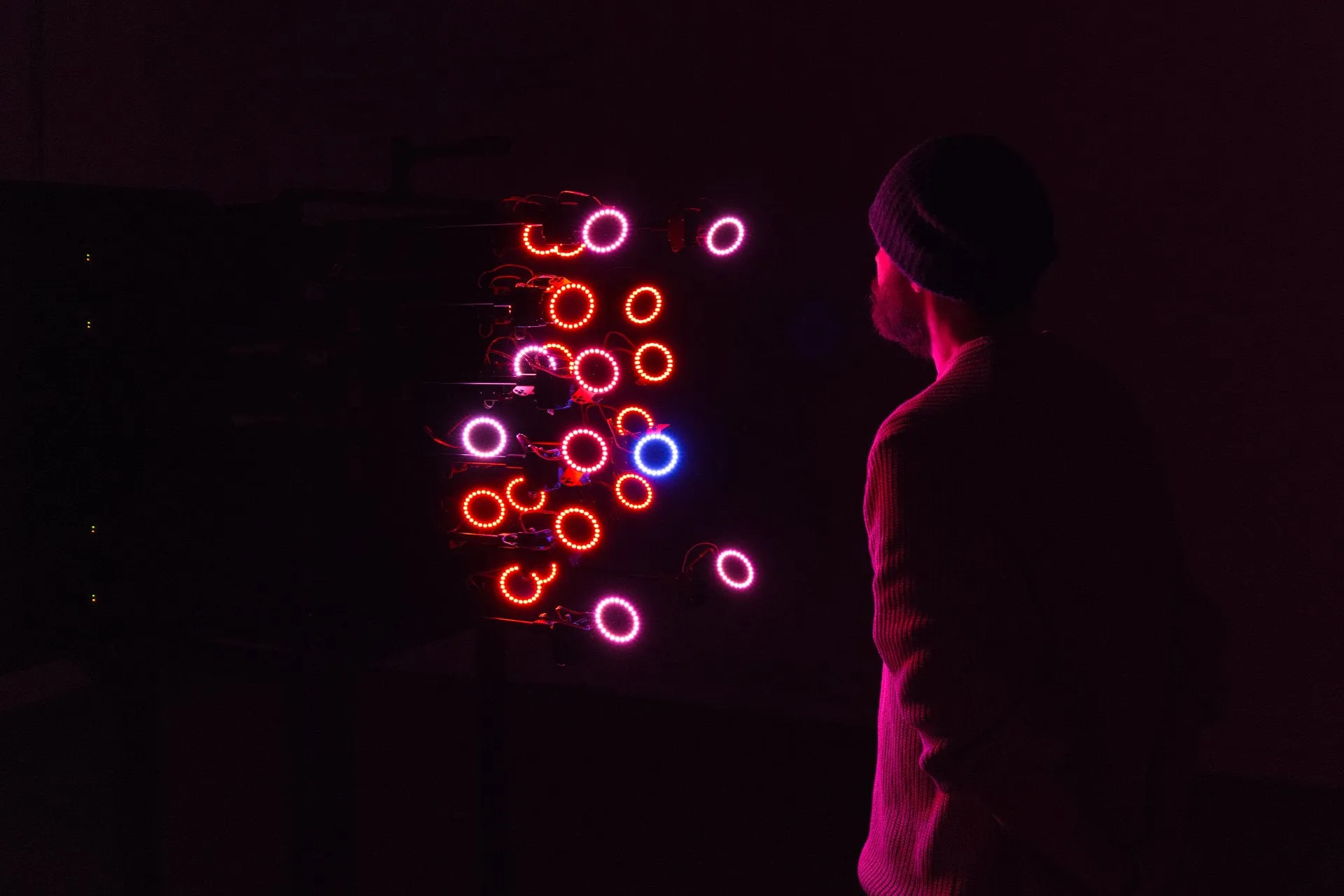 Un visitante con gorro observa de perfil los anillos de luz roja y blanca que se agrupan frente a su cara