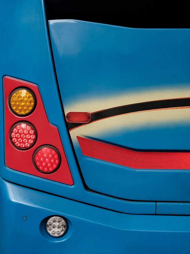 Trasera azul de un autobús con una franja crema curvada, una línea roja y un grupo de pilotos rojos y naranjas