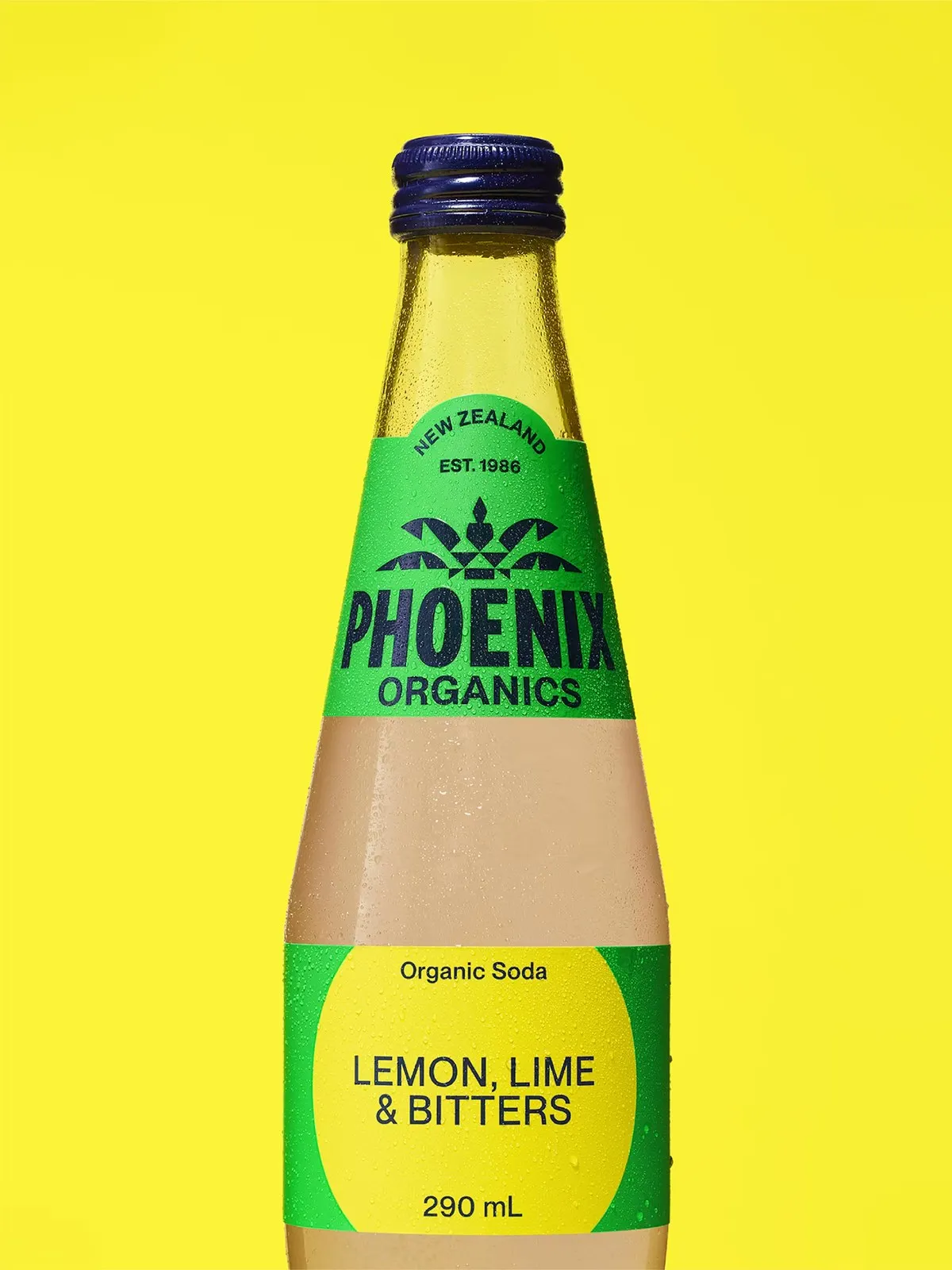 Botella de refresco Phoenix Organics de limón, lima y amargo con etiqueta verde y amarilla sobre fondo amarillo