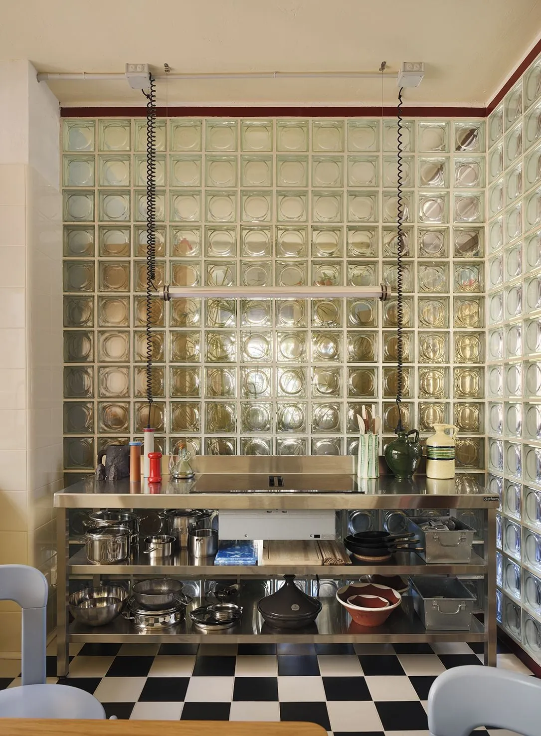Cocina con suelo de ajedrez en blanco y negro, isla de acero inoxidable y pared de bloques de vidrio