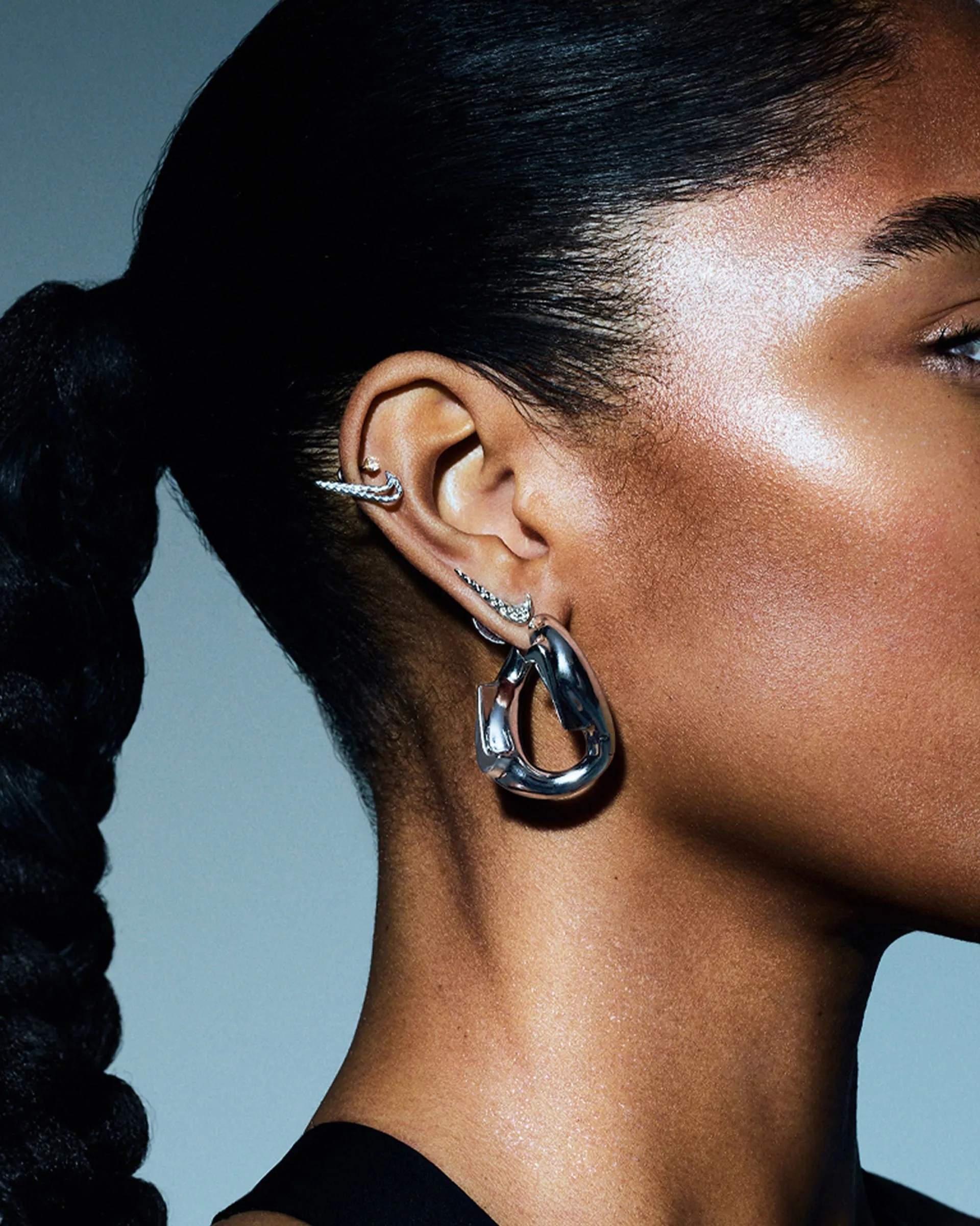 Perfil de una mujer con trenza larga, con un aro plateado de eslabón grande y un ear cuff en la oreja