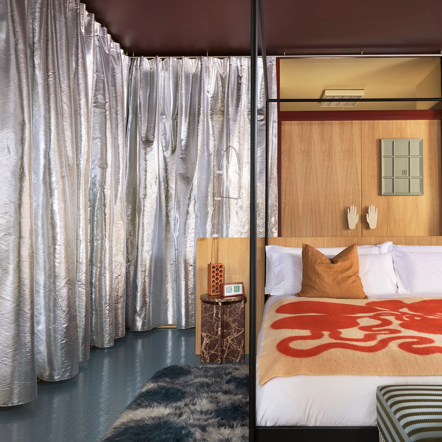 Dormitorio con cortinas plateadas, cama con dosel negro, panel de madera y manta naranja con un dibujo ondulado