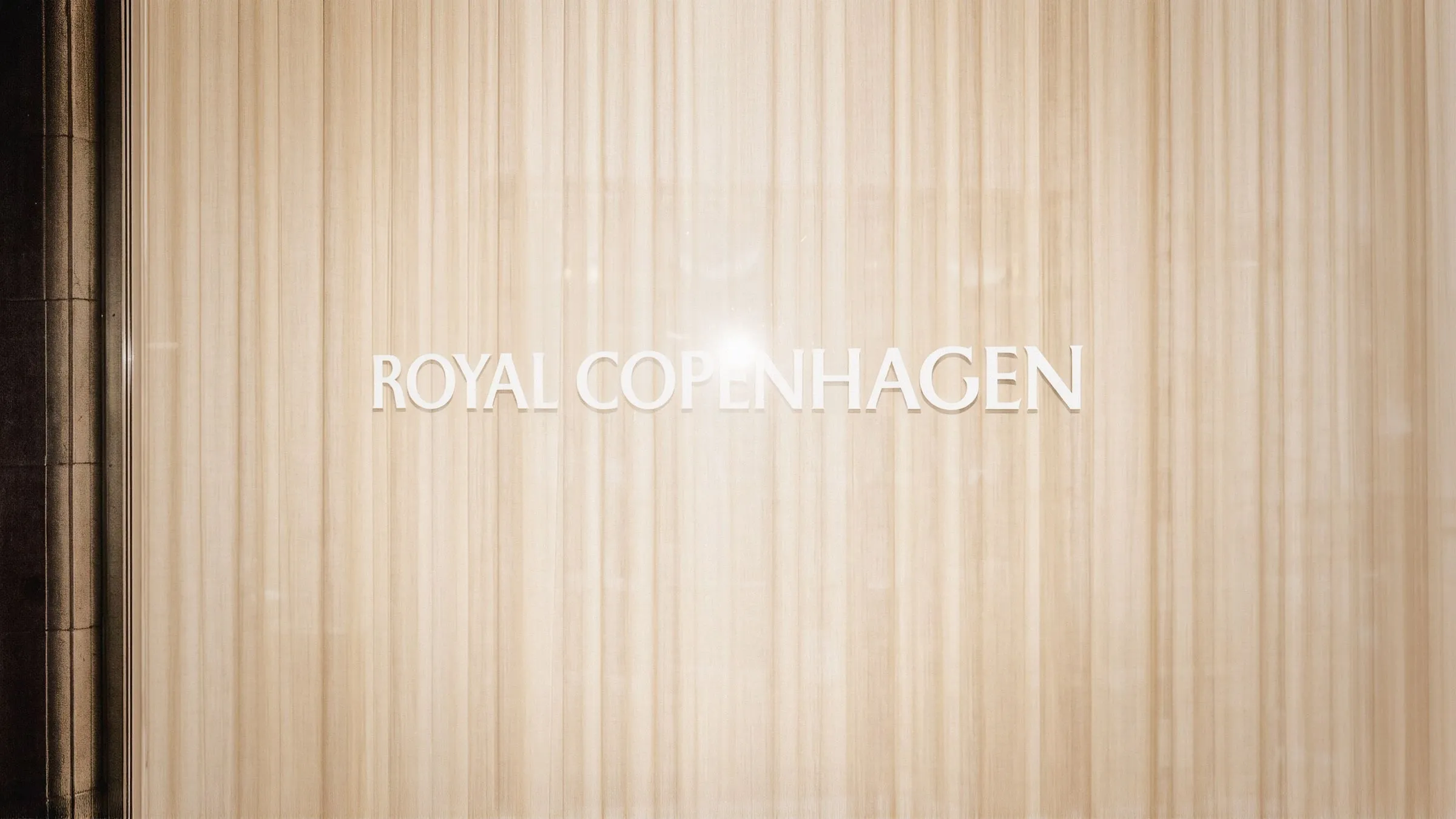 Logotipo de Royal Copenhagen en letras blancas sobre una cortina de lamas de madera clara