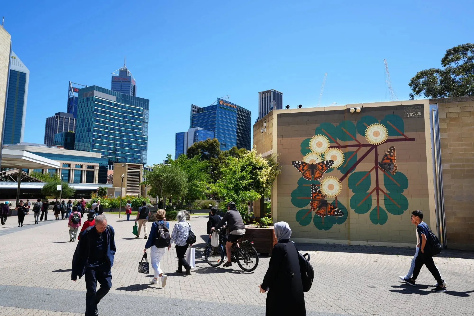 Mural de mariposas naranjas y hojas verdes en una pared del centro de Perth, con peatones delante
