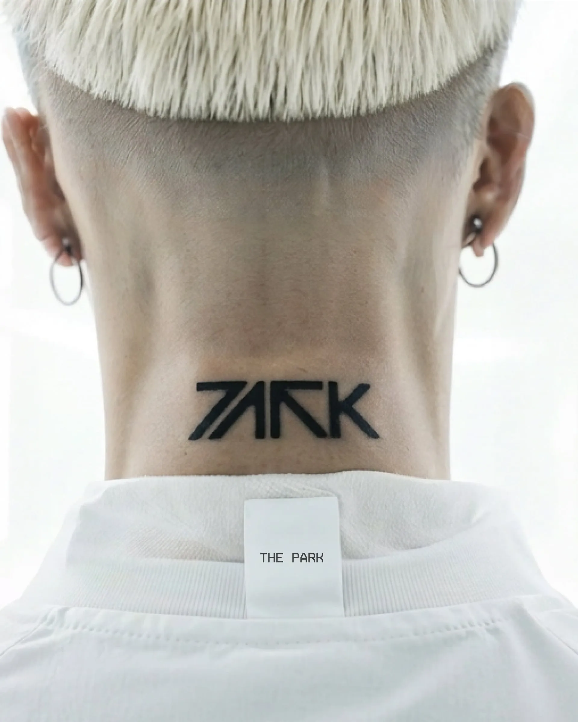 Nuca de una persona con el logotipo de PARK tatuado sobre la piel, junto a la etiqueta interior de una camiseta blanca