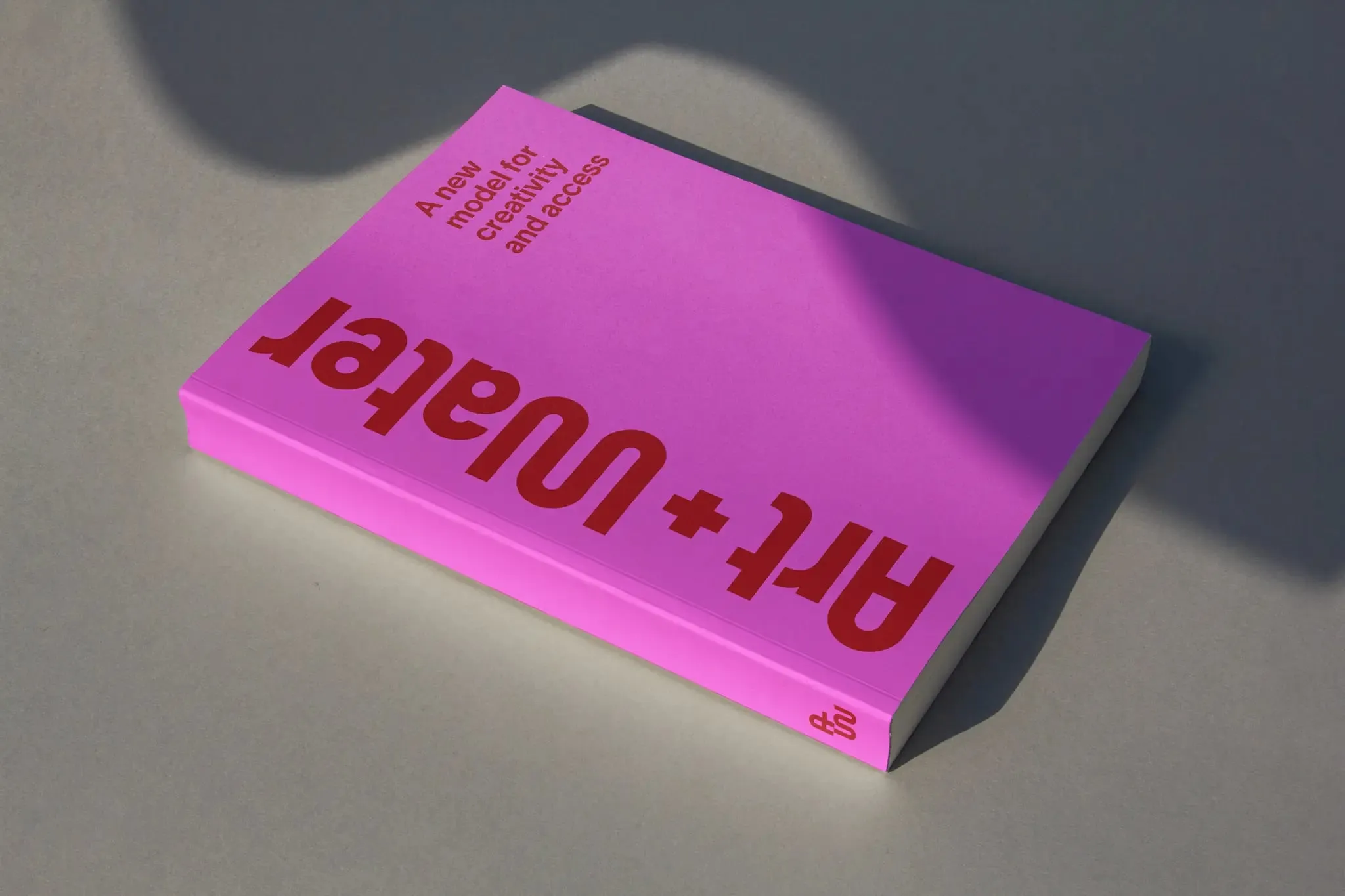 Libro de tapa rosa chicle tumbado sobre fondo gris, con el título «Art + Water» en letras onduladas rojas