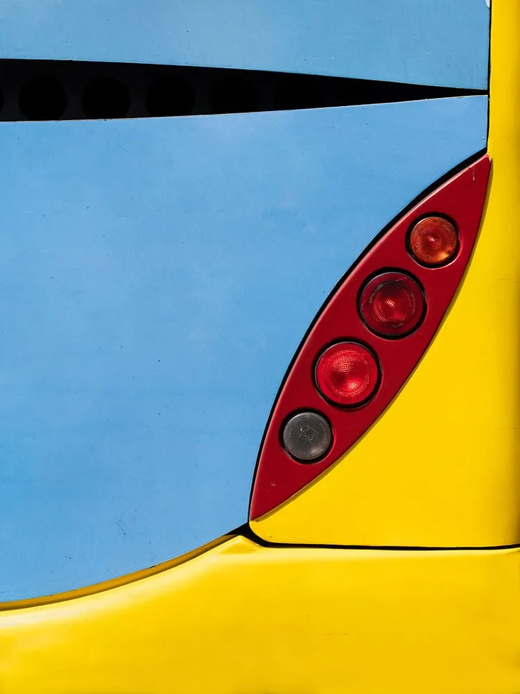 Trasera de autobús pintada de azul claro arriba y amarillo abajo, con un piloto rojo en forma de gota a la derecha
