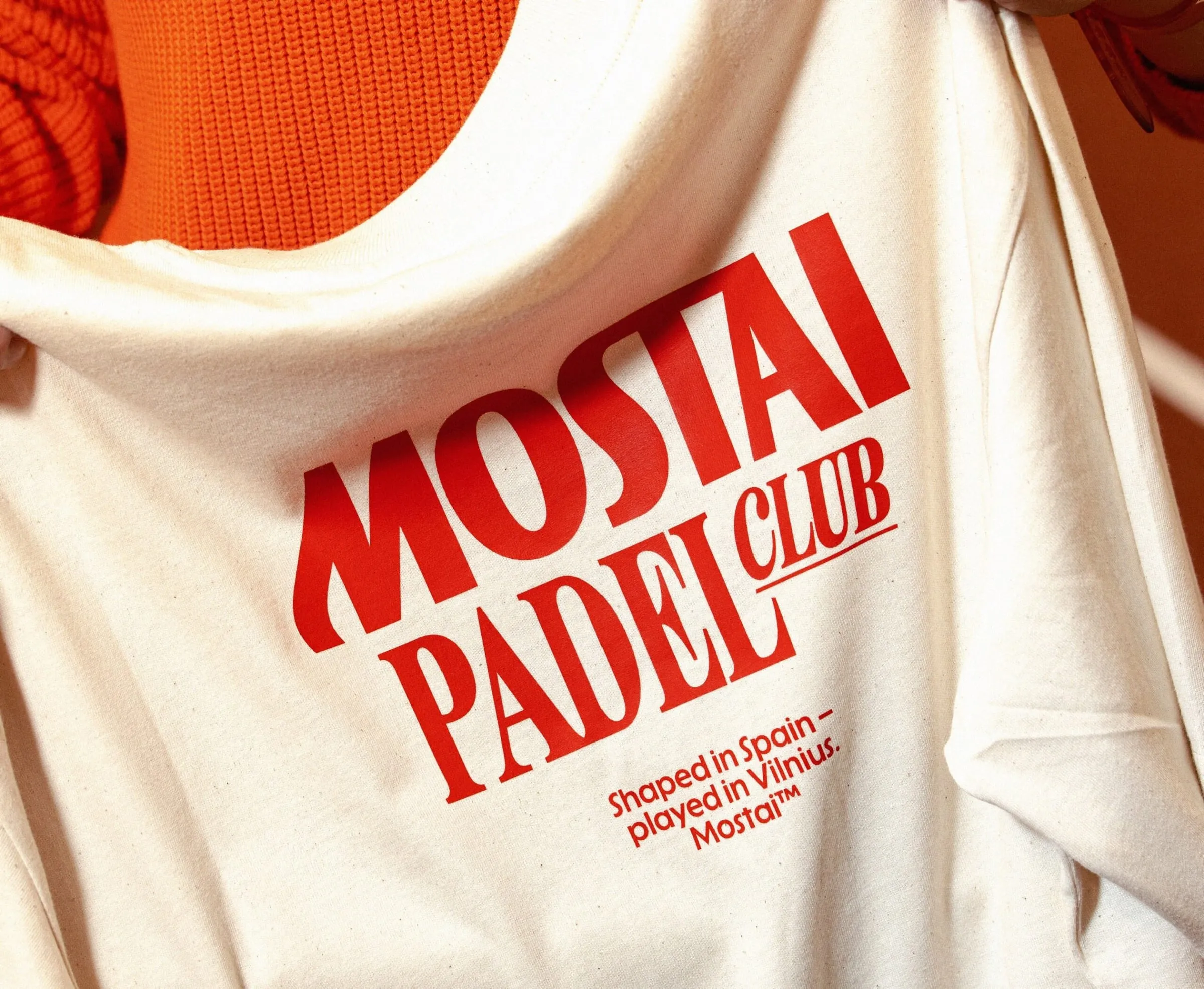 Camiseta crema con el texto «Mostai Padel Club» en rojo y la frase «Shaped in Spain – played in Vilnius»