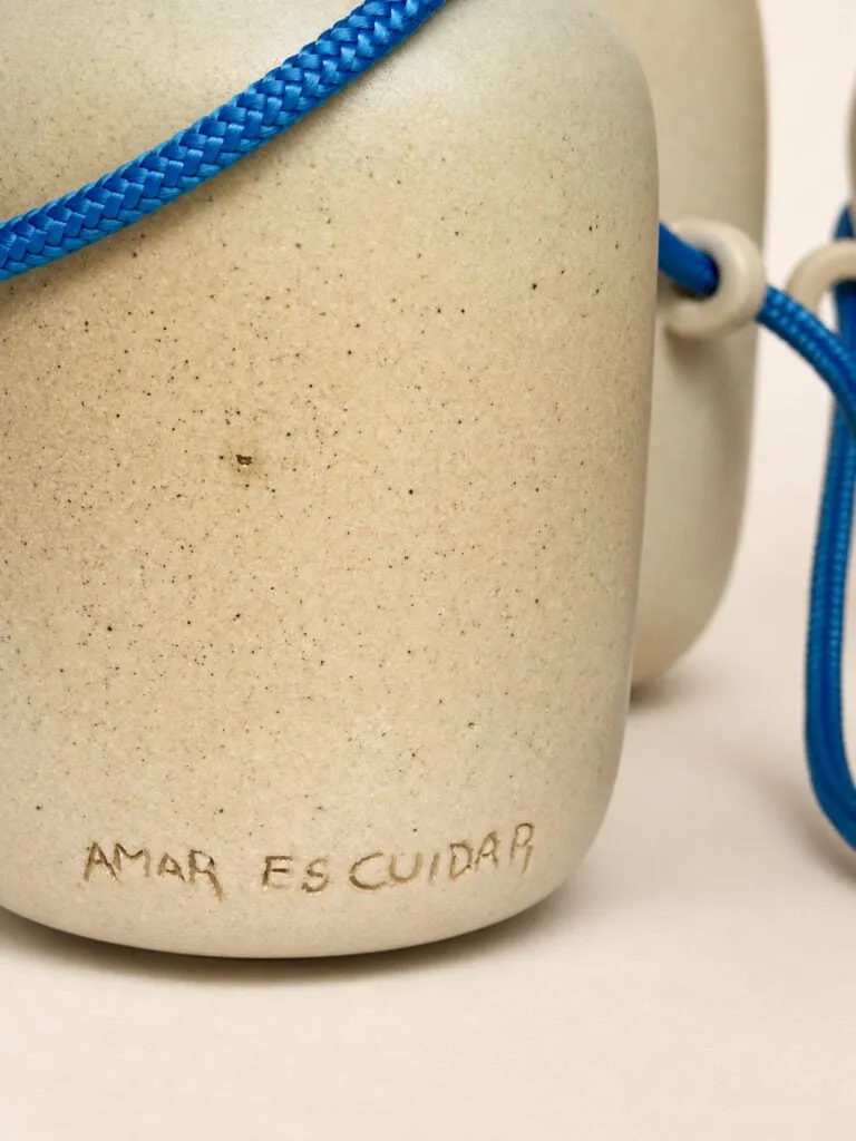 Vasija de gres con la frase «Amar es cuidar» grabada a mano, junto a otra pieza unida por un cordón azul a través de pequeñas asas cerámicas