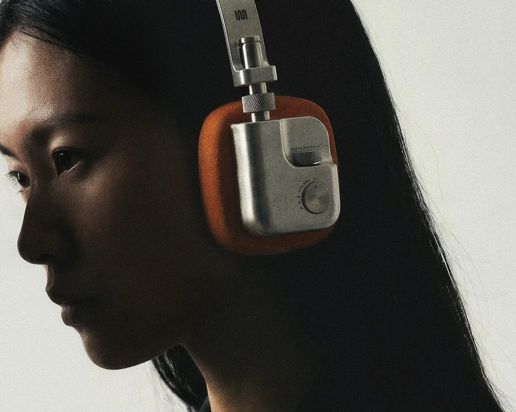 Primer plano del rostro de una mujer de perfil con el auricular de aluminio y tela naranja, con la rueda de graves y agudos junto a la oreja