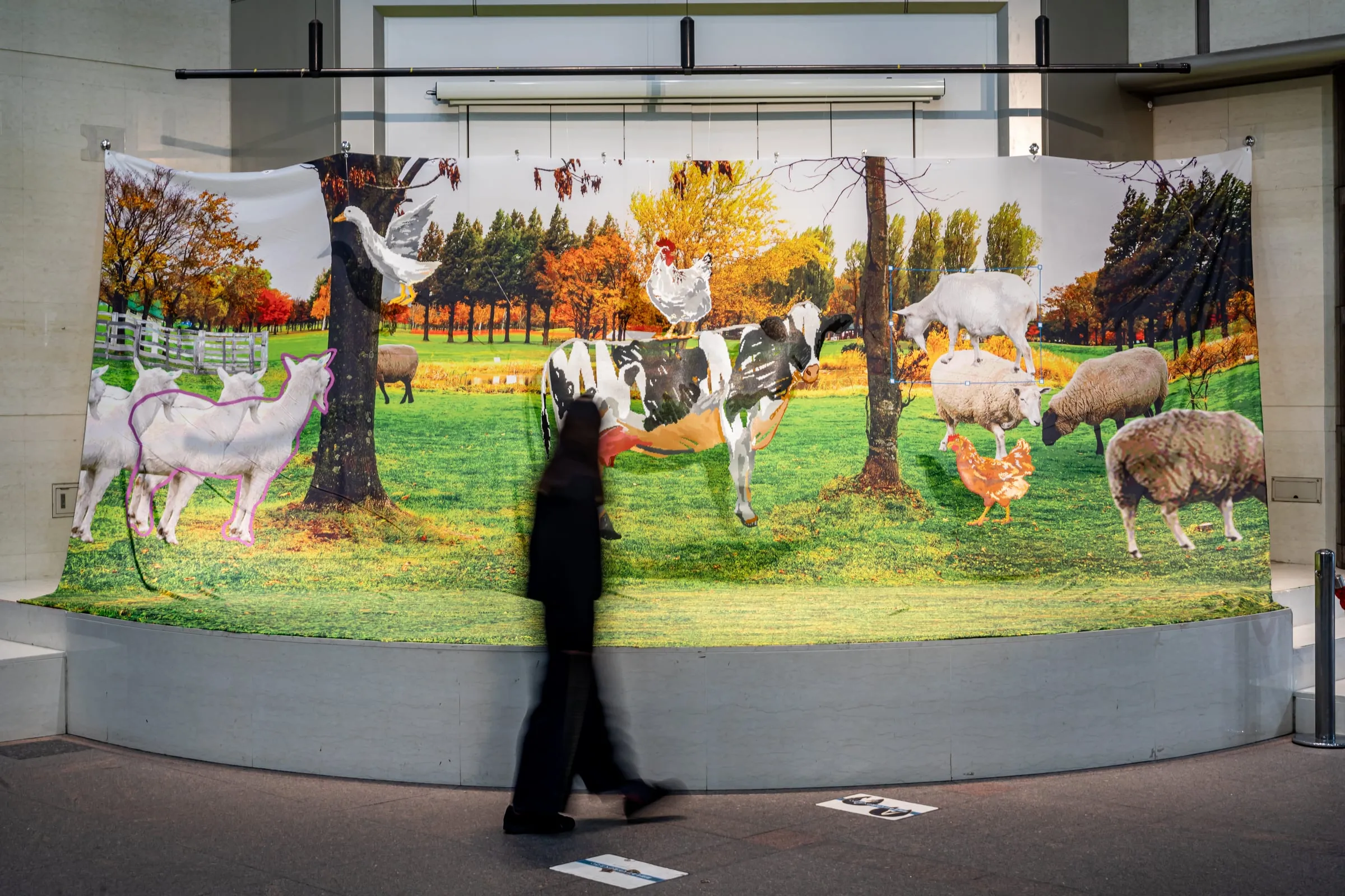 Mural de una granja en otoño con ovejas, cabras, gallinas y una vaca, visto desde el pasillo, con una persona caminando borrosa delante