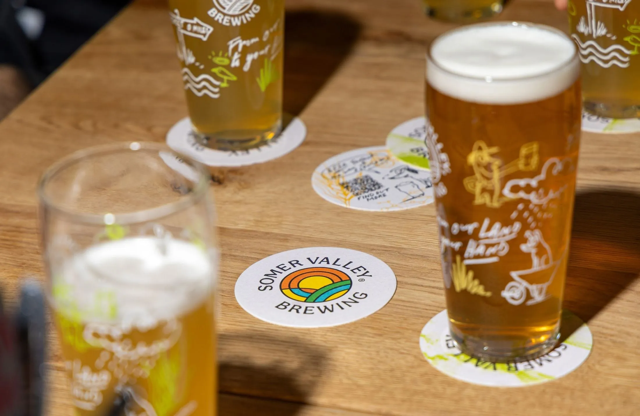 Posavasos y vasos de cerveza con dibujos blancos de granja sobre una mesa de madera