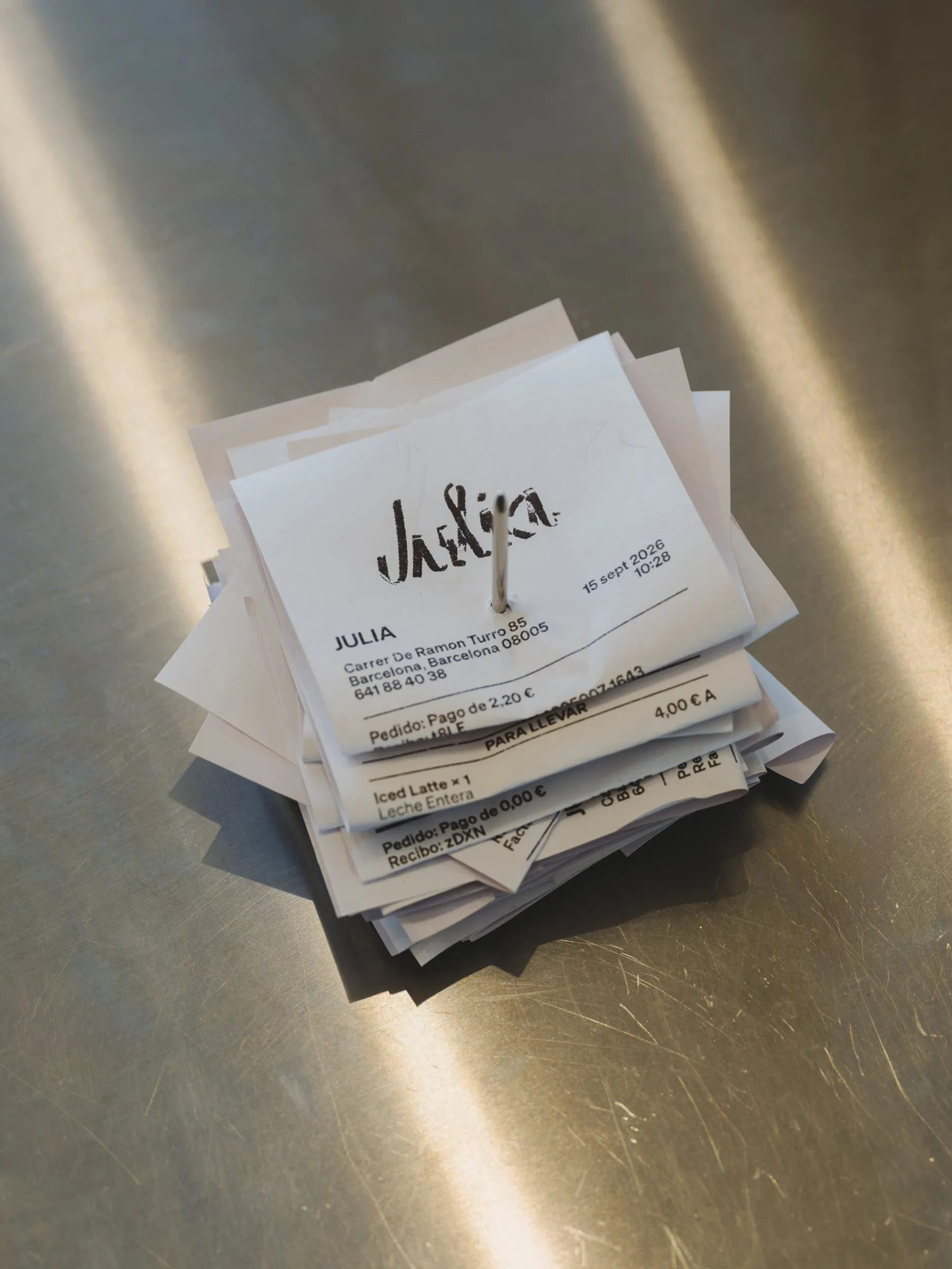 Montón de tickets con el logotipo de Julia impreso en negro, atravesados por un pincho metálico sobre una encimera de acero