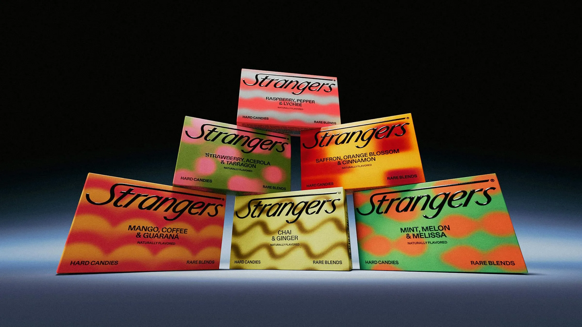 Filas de cajas de Strangers bajo un expositor negro con el texto de saludo, en amarillo, rojo, rosa y verde