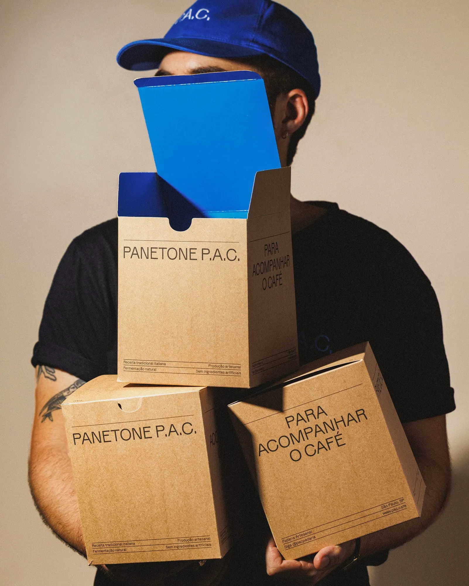 Persona con gorra azul sosteniendo tres cajas de cartón kraft con el texto «Panetone P.A.C.»