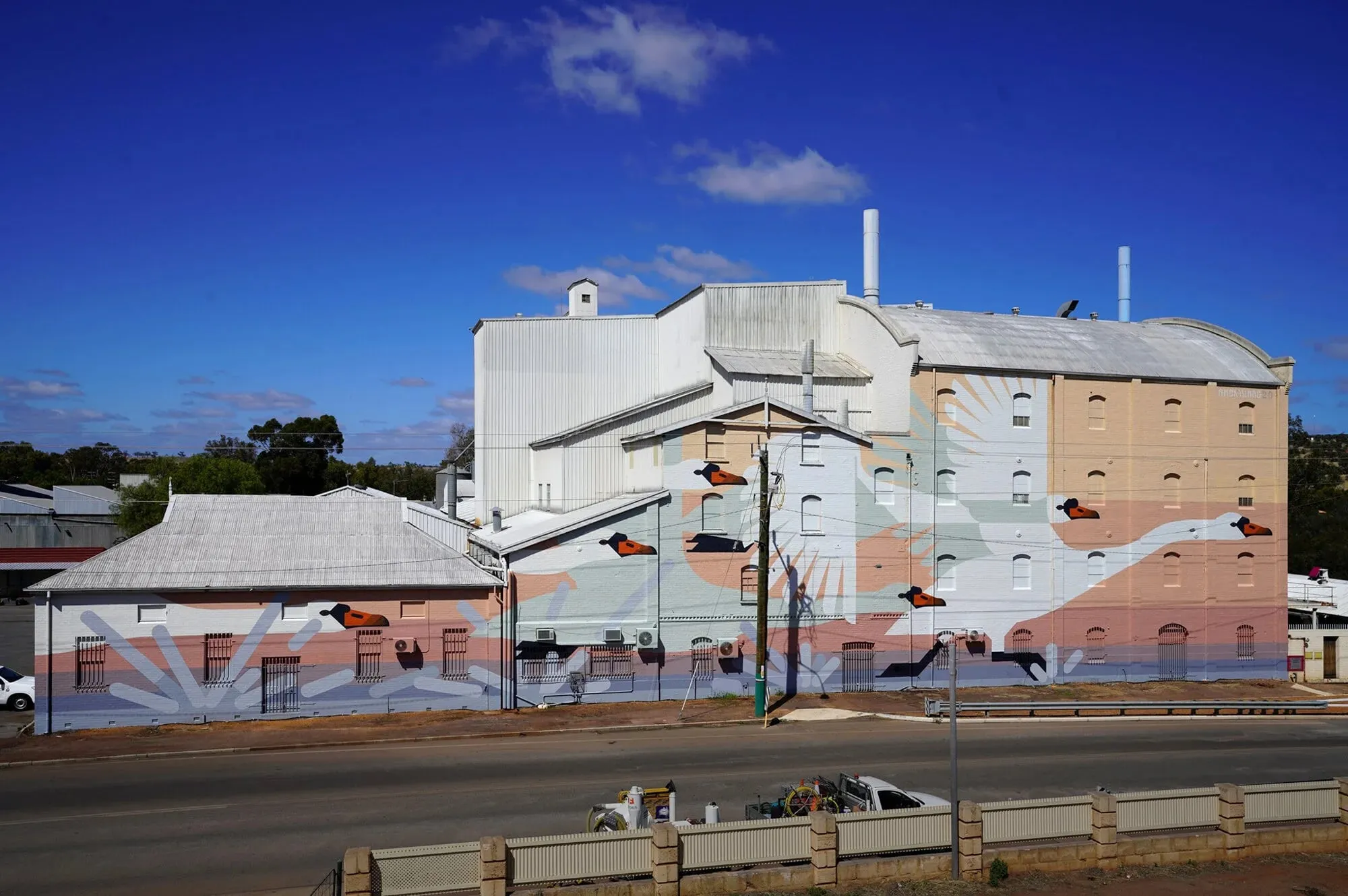 Mural de cisnes geométricos sobre un gran muro industrial de Northam