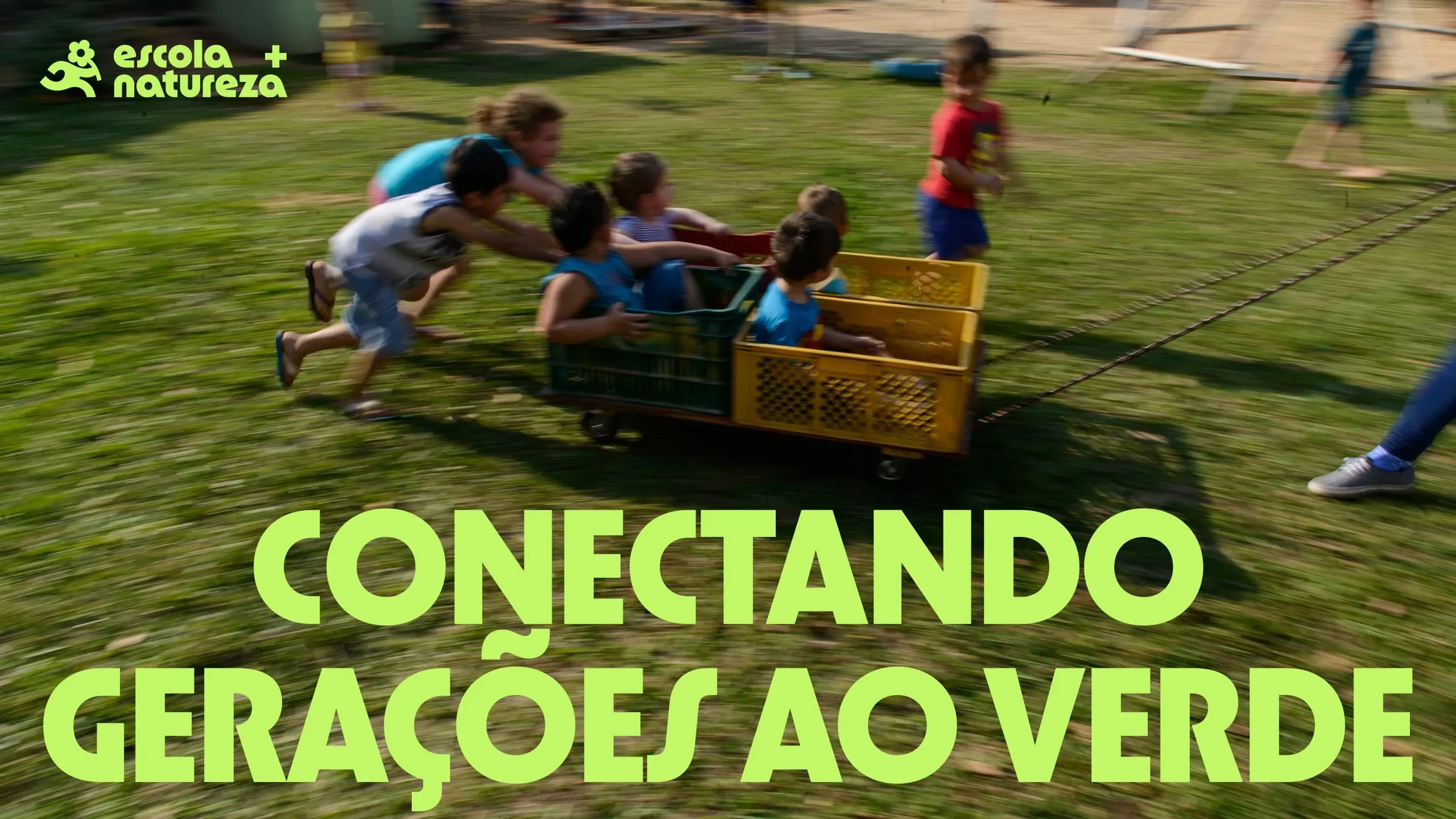 Niños empujan un carro amarillo sobre el césped bajo el lema «Conectando gerações ao verde» y el logo de Escola + Natureza