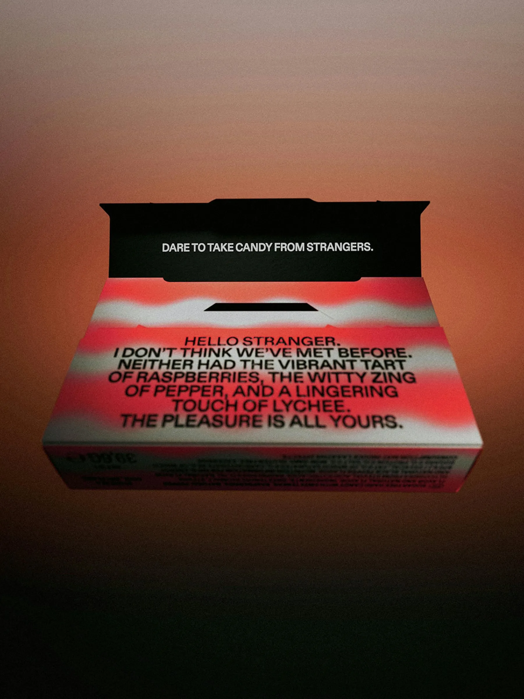 Caja abierta de Strangers de frambuesa, pimienta y lichi, con el saludo impreso en negro sobre el interior rosa y blanco