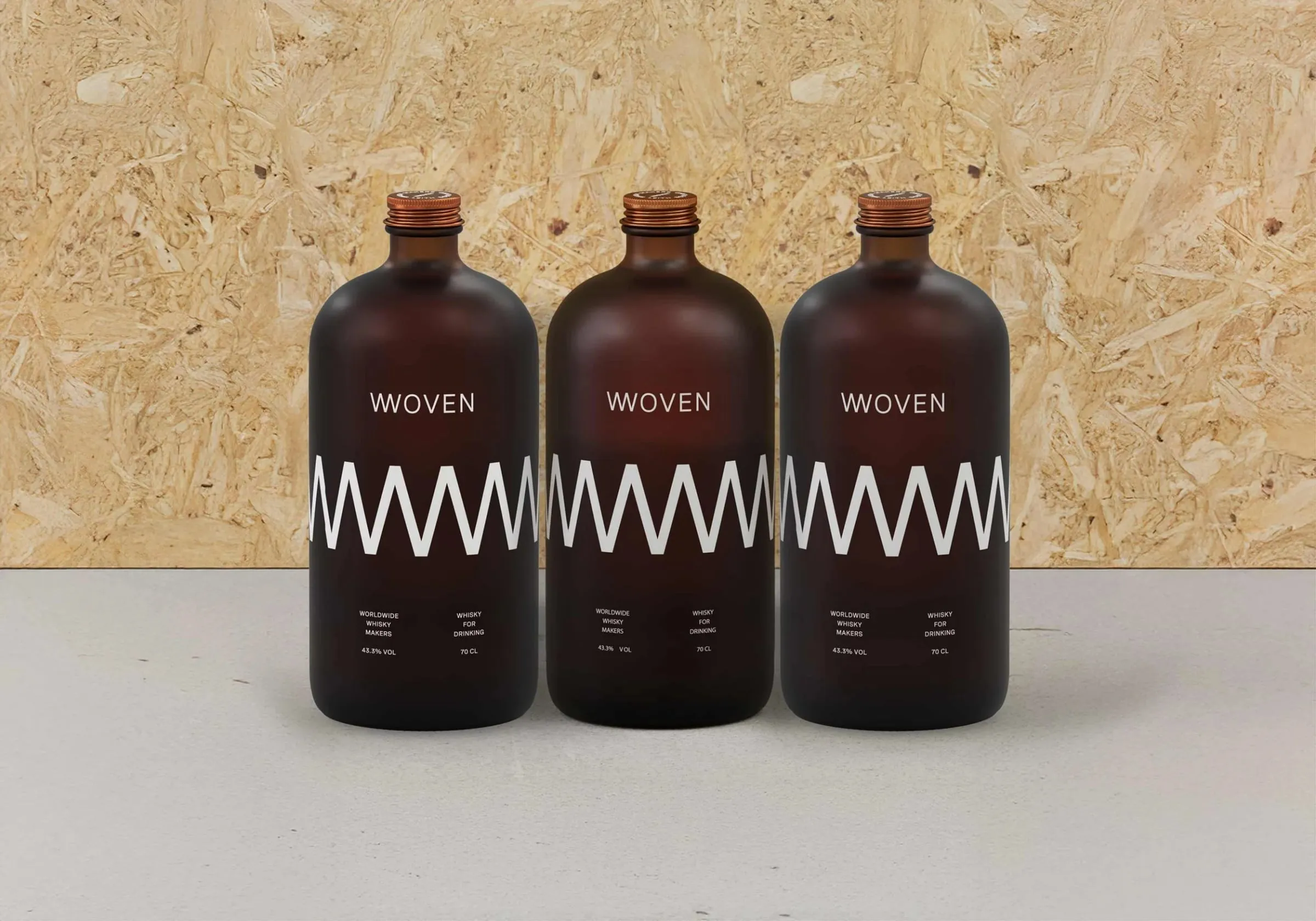 Tres botellas marrones de Woven con una banda blanca en zigzag alrededor del cuerpo y tapón de cobre